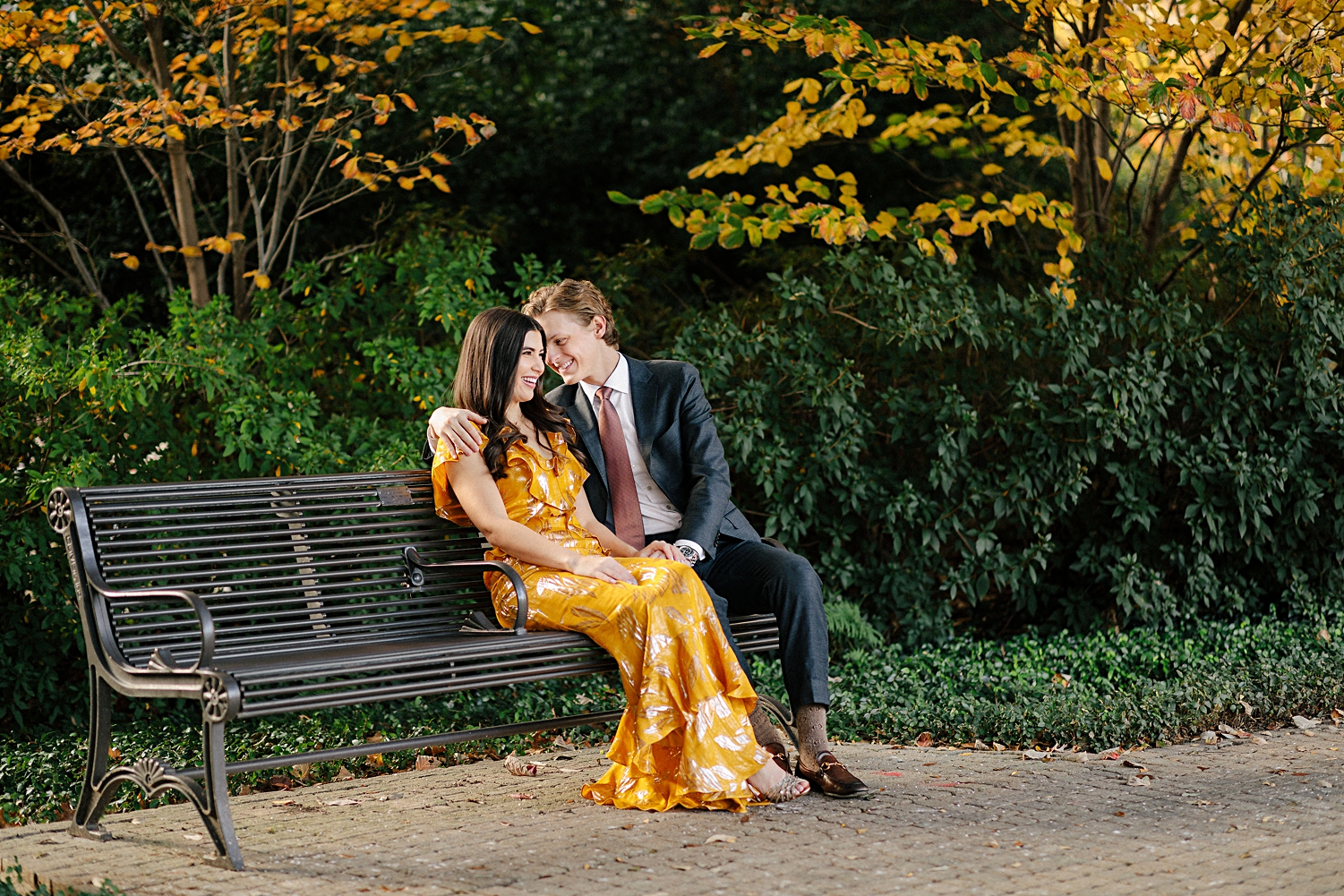 man laughing with woman in yellow dress while sitting on park bench