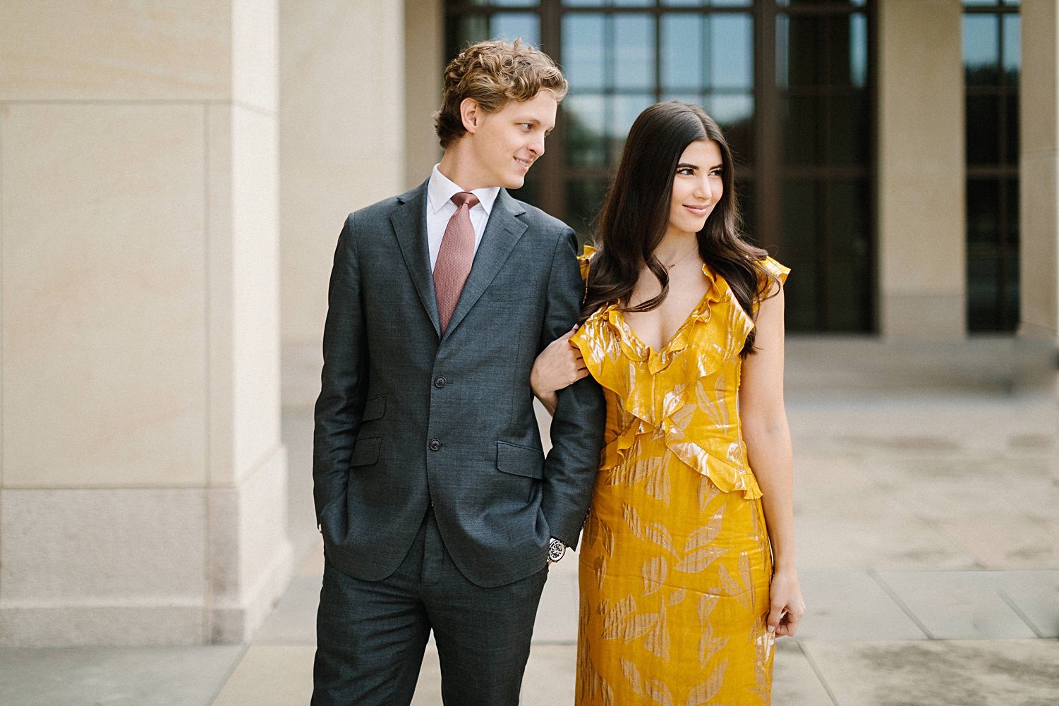 woman in yellow dress standing with man in suit in front of concrete pillars