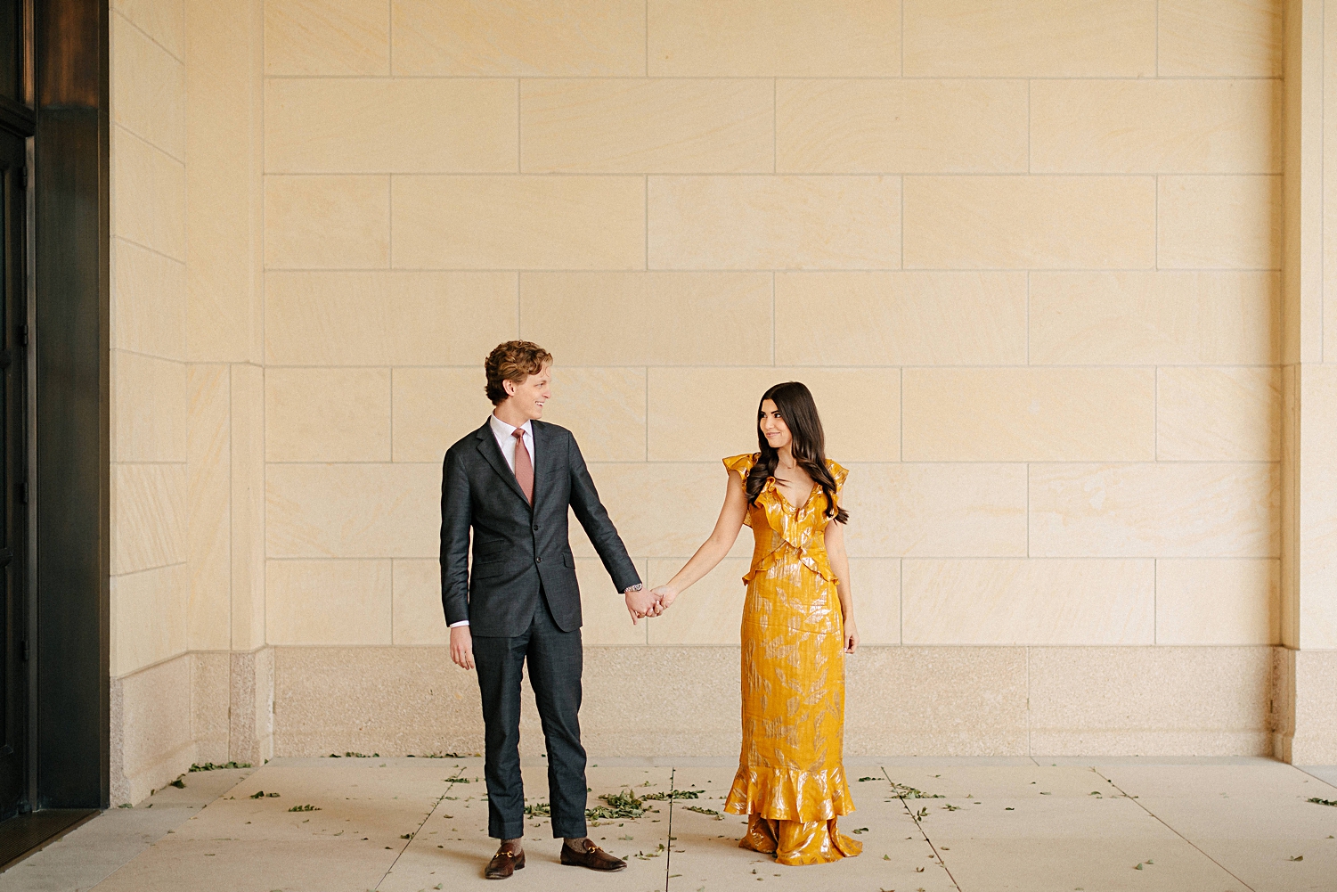woman in yellow dress holding hands with man in suit in front of stone wall engagement 