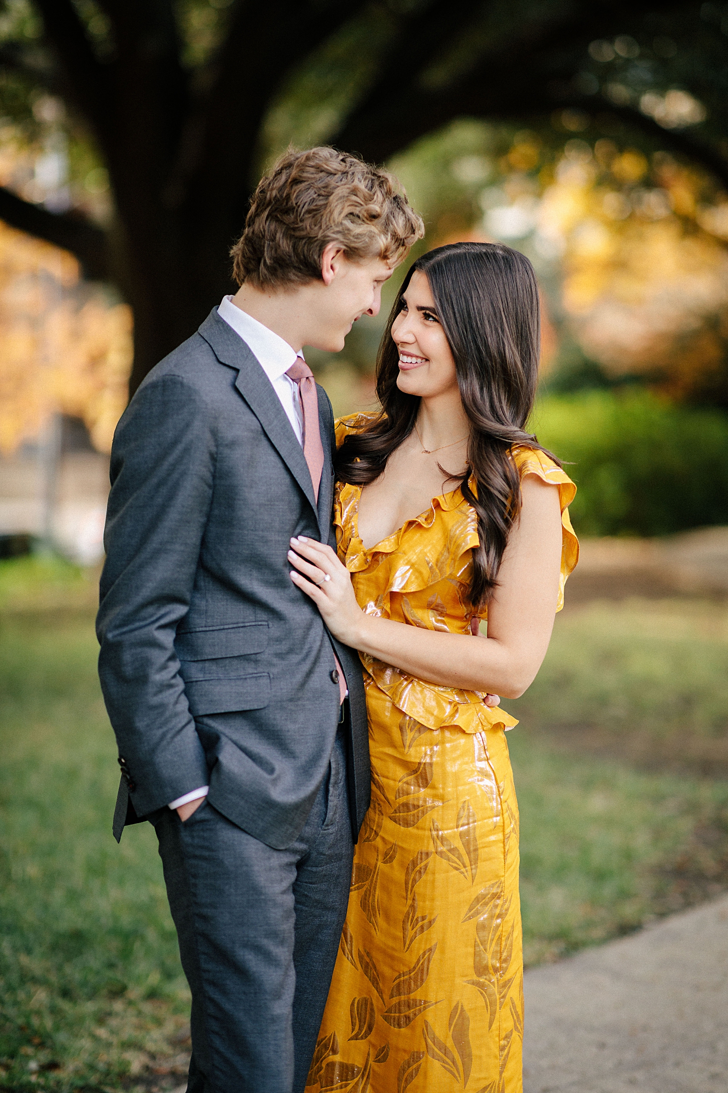 woman in yellow dress standing with man in suit in park