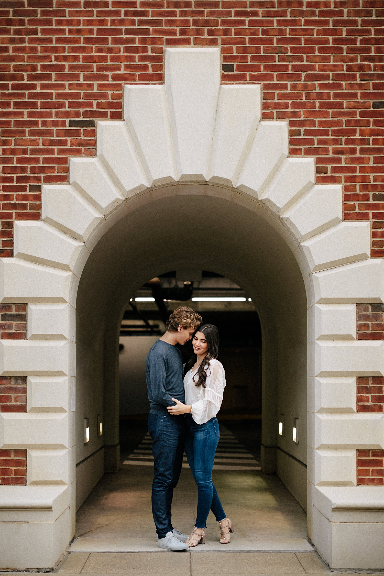 couple hugging by meadows museum red brick and stone entrance way on SMU dallas campus engagement