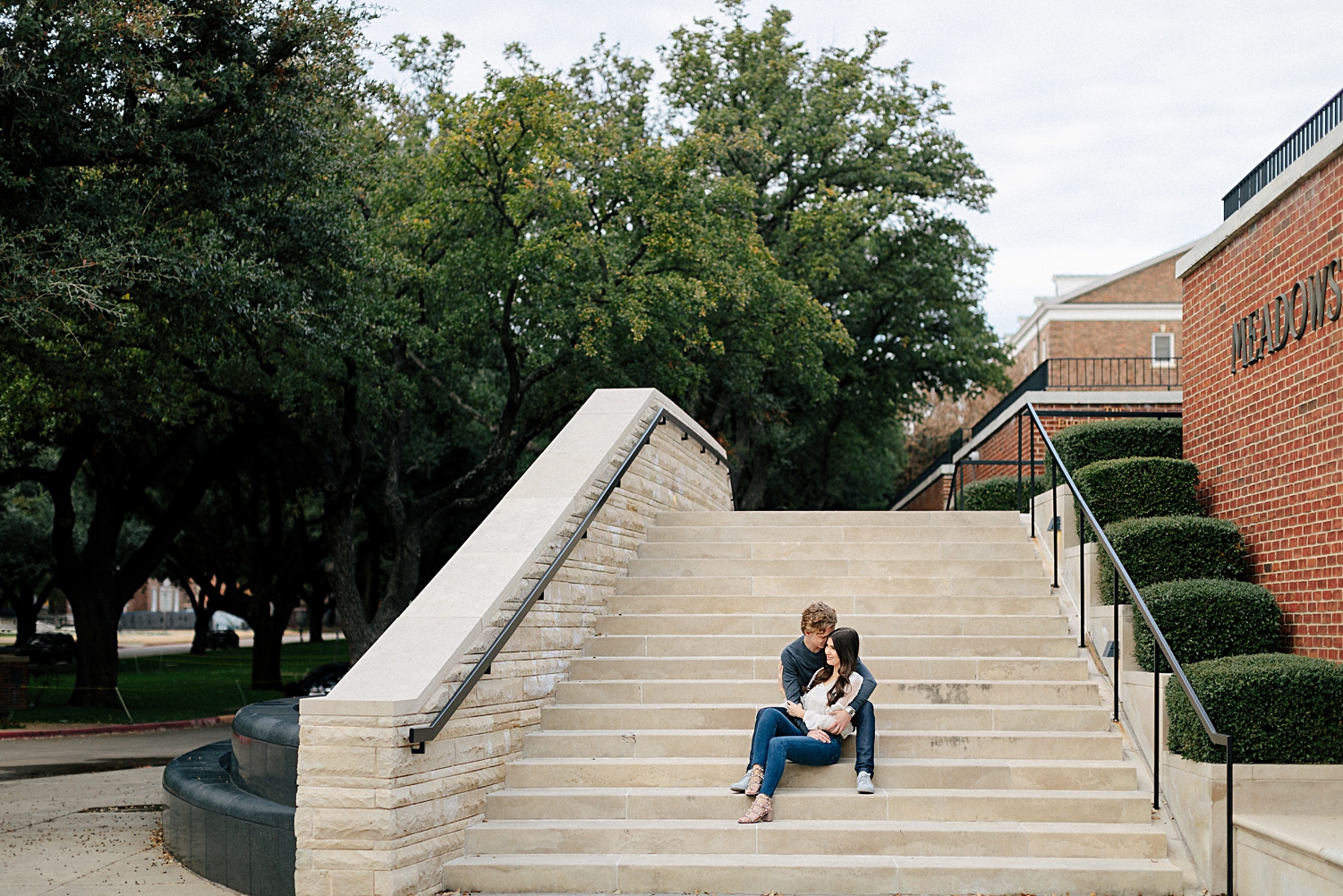 couple sitting together on steps in front of meadows museum red brick building on SMU dallas campus engagement