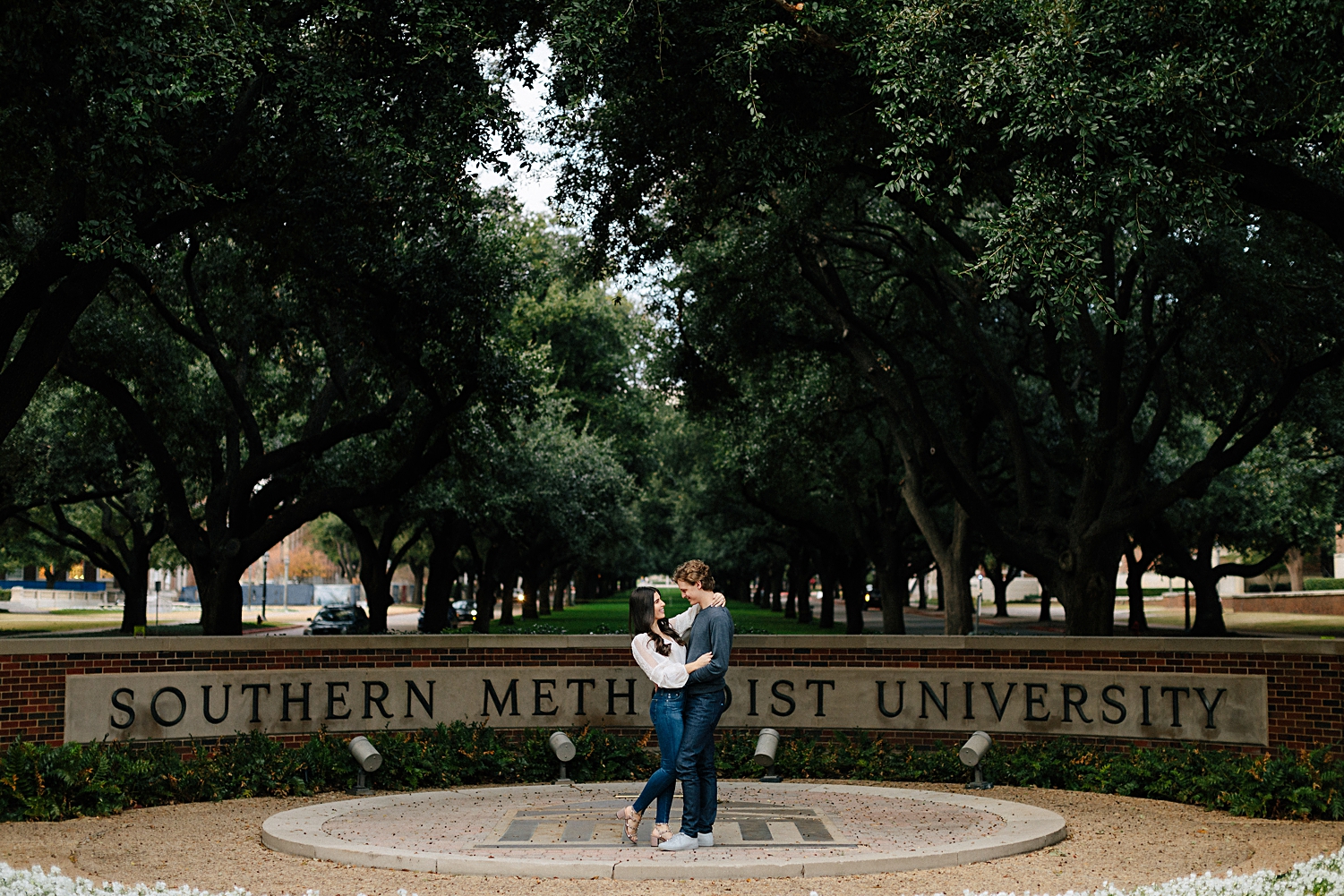 Couple hugging and smiling at engagement in front of Southern Methodist University SMU campus entrance sign Dallas, texas