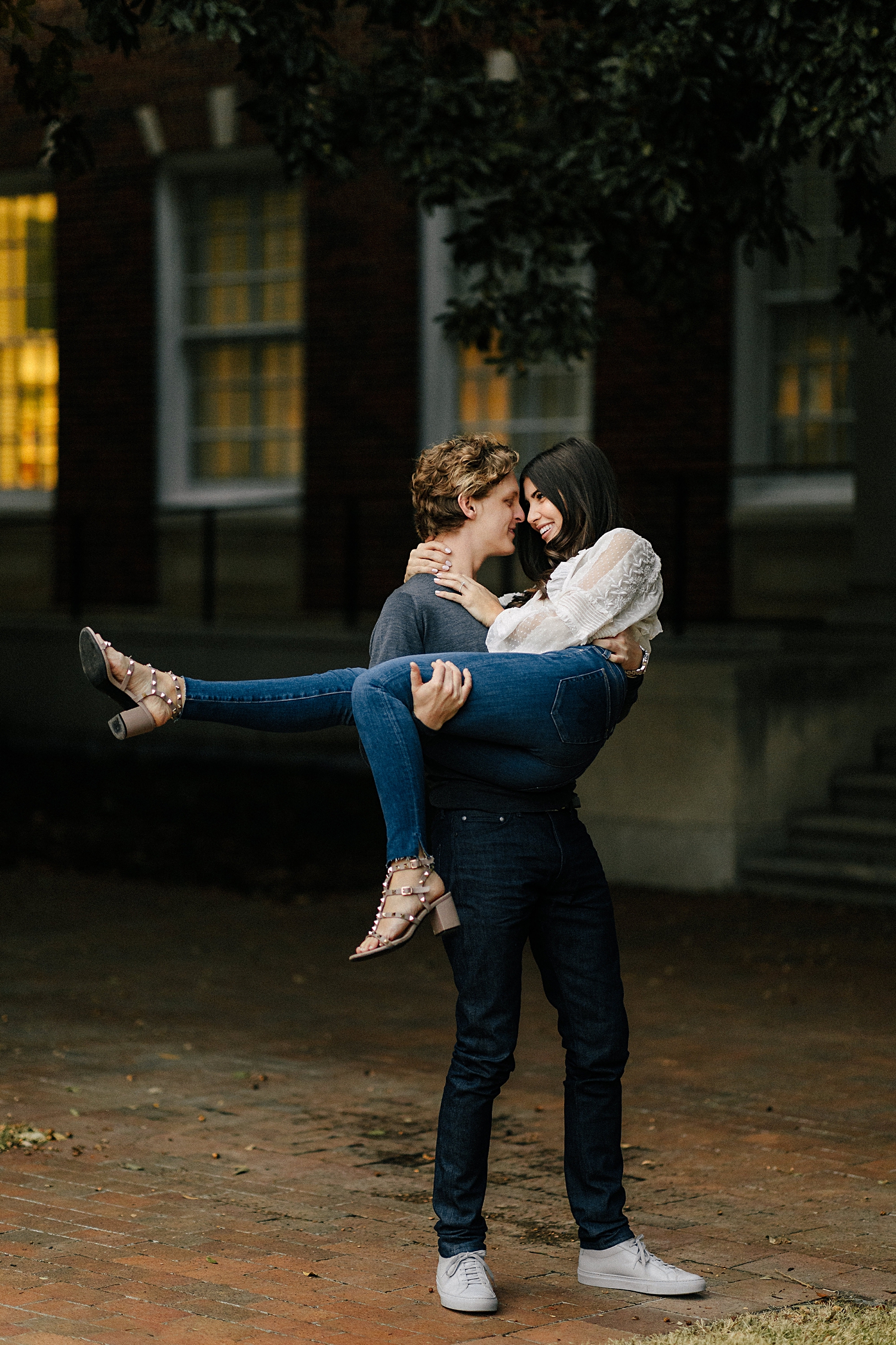man holding girl in arms smiling with leg kicked out during engagement