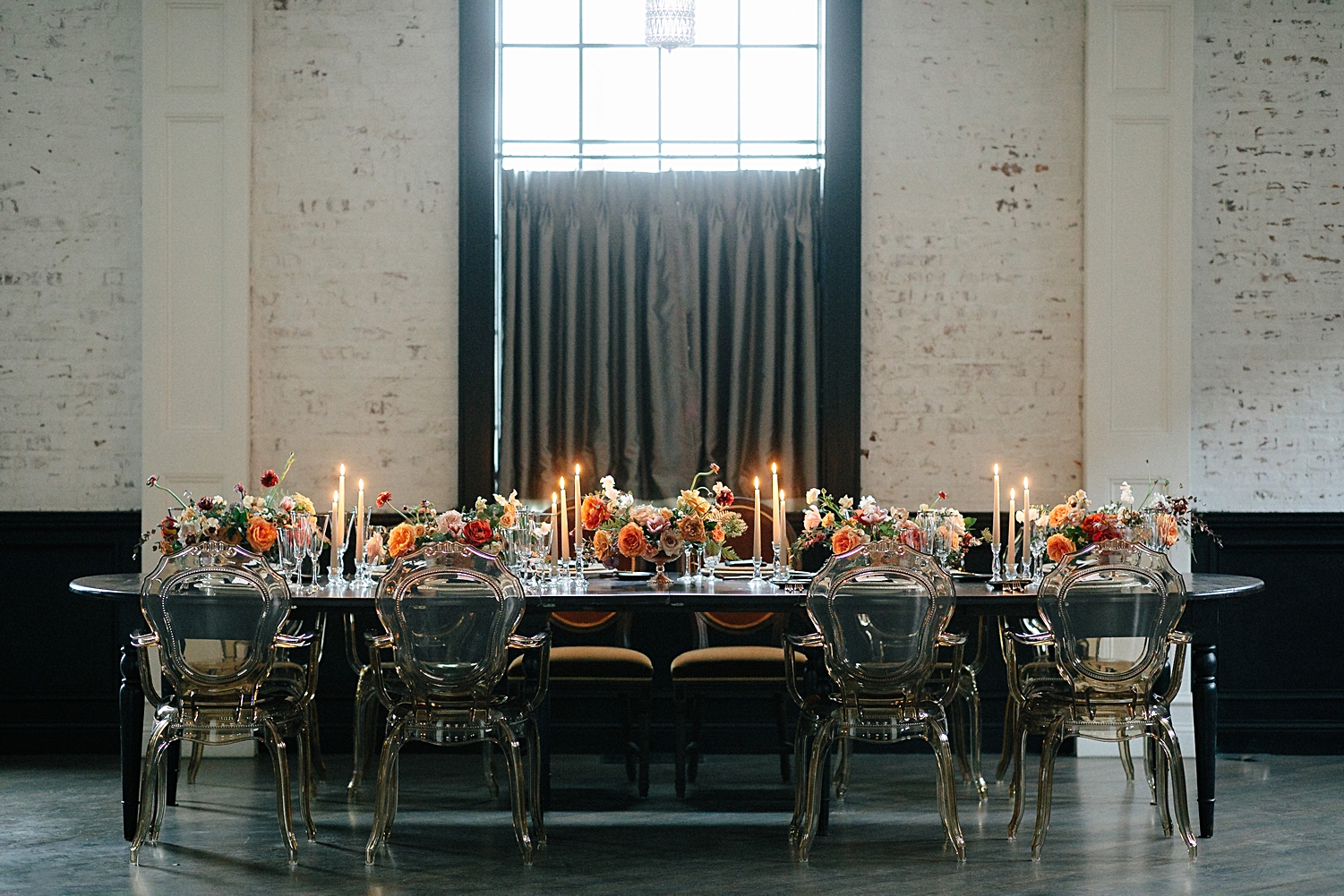 wedding reception table with candles orange, red florals in front of window and white brick wall