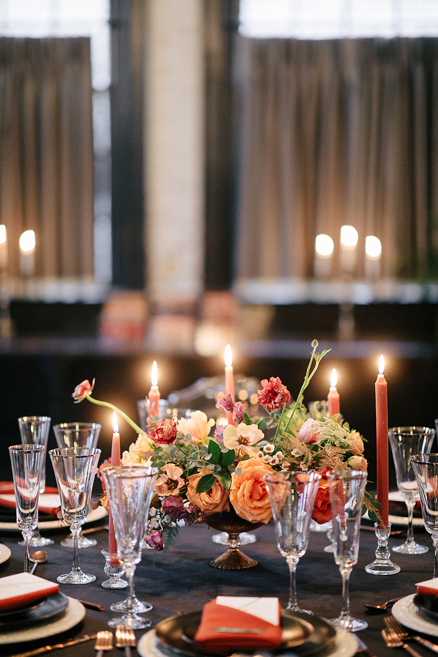 wedding reception table with candles orange, red florals in front of windows