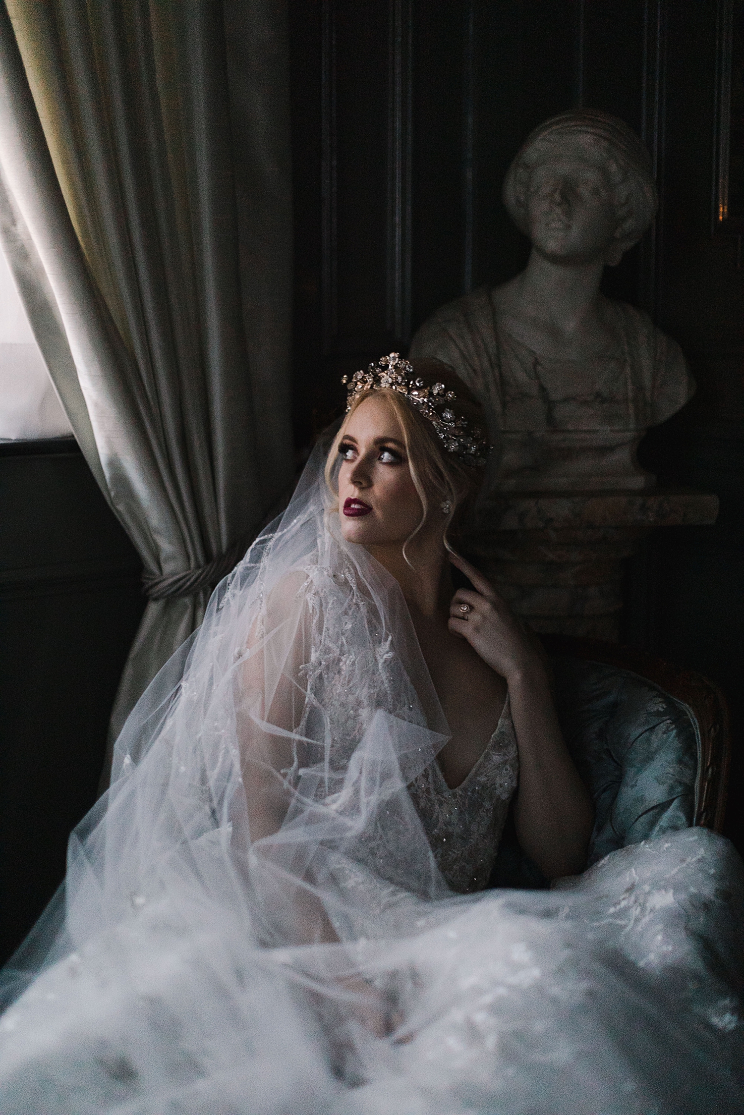bride in wedding dress, crown, veil laying by window in dark room