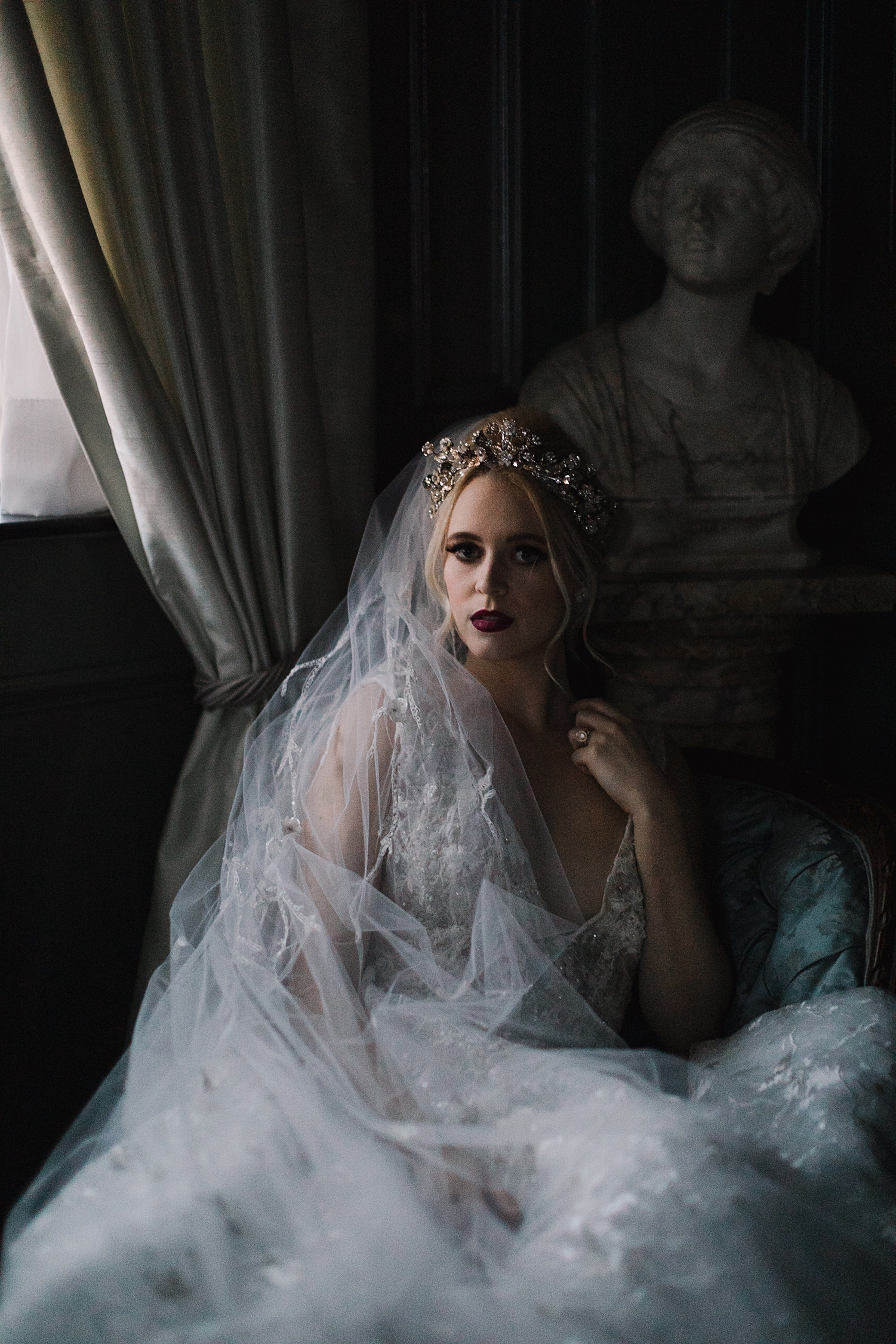 bride in wedding dress, tiara, veil laying by window in dark room
