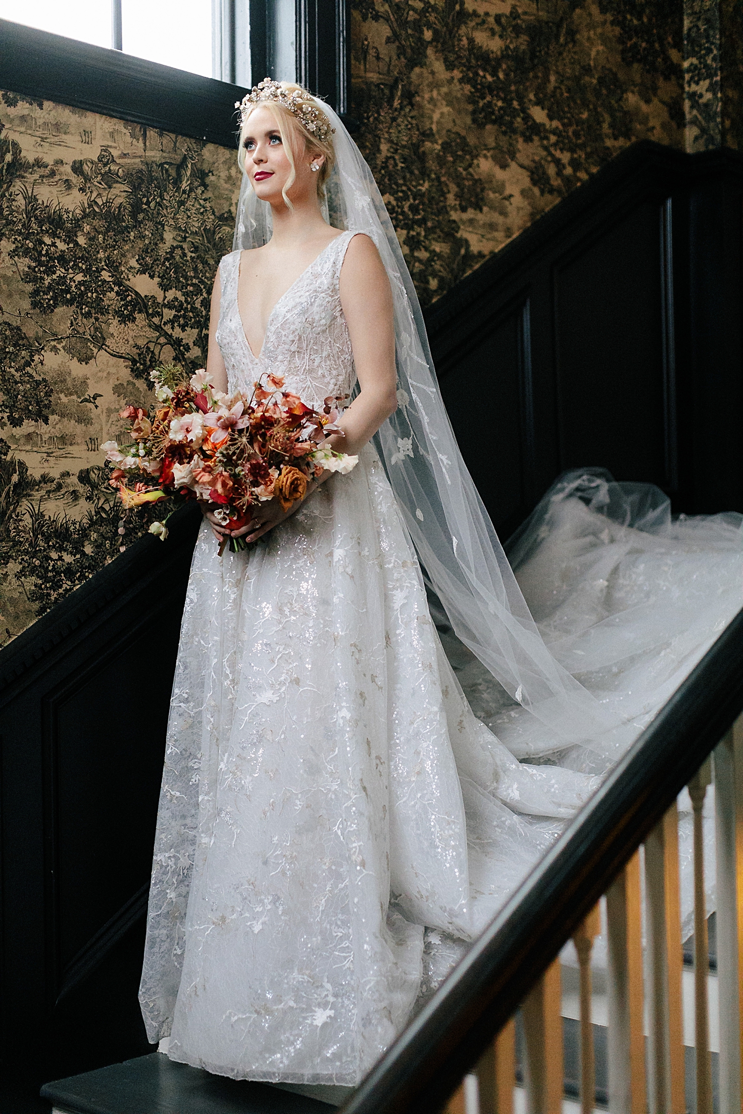 bride in shimmering white wedding dress and veil standing on staircase holding orange bridal bouquet at The Mason Dallas