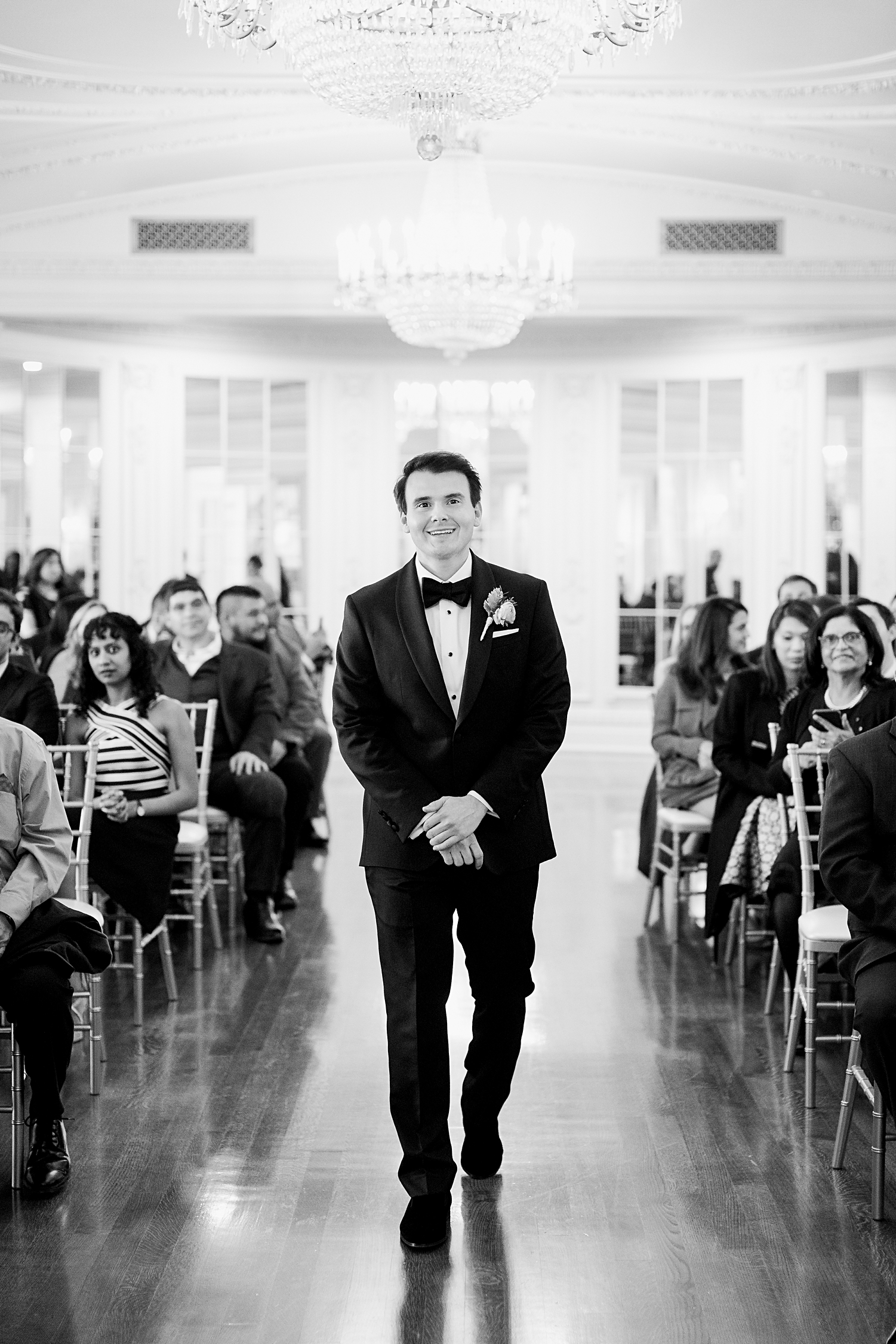Indoor wedding ceremony groom walking down aisle smiling black and white