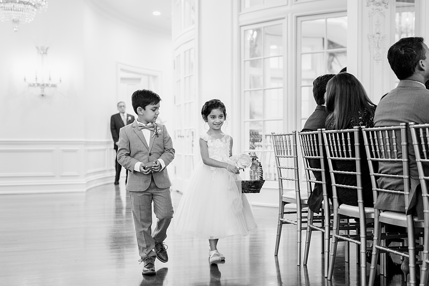 Indoor wedding ceremony flower girl and ring bearer walking down aisle smiling black and white