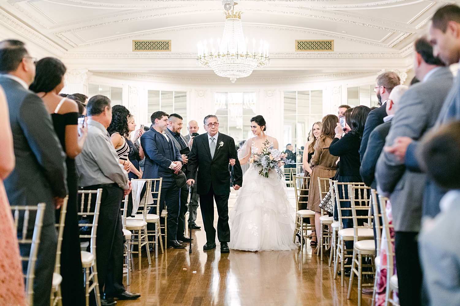 Indoor wedding ceremony bride and father walking down aisle with bouquet