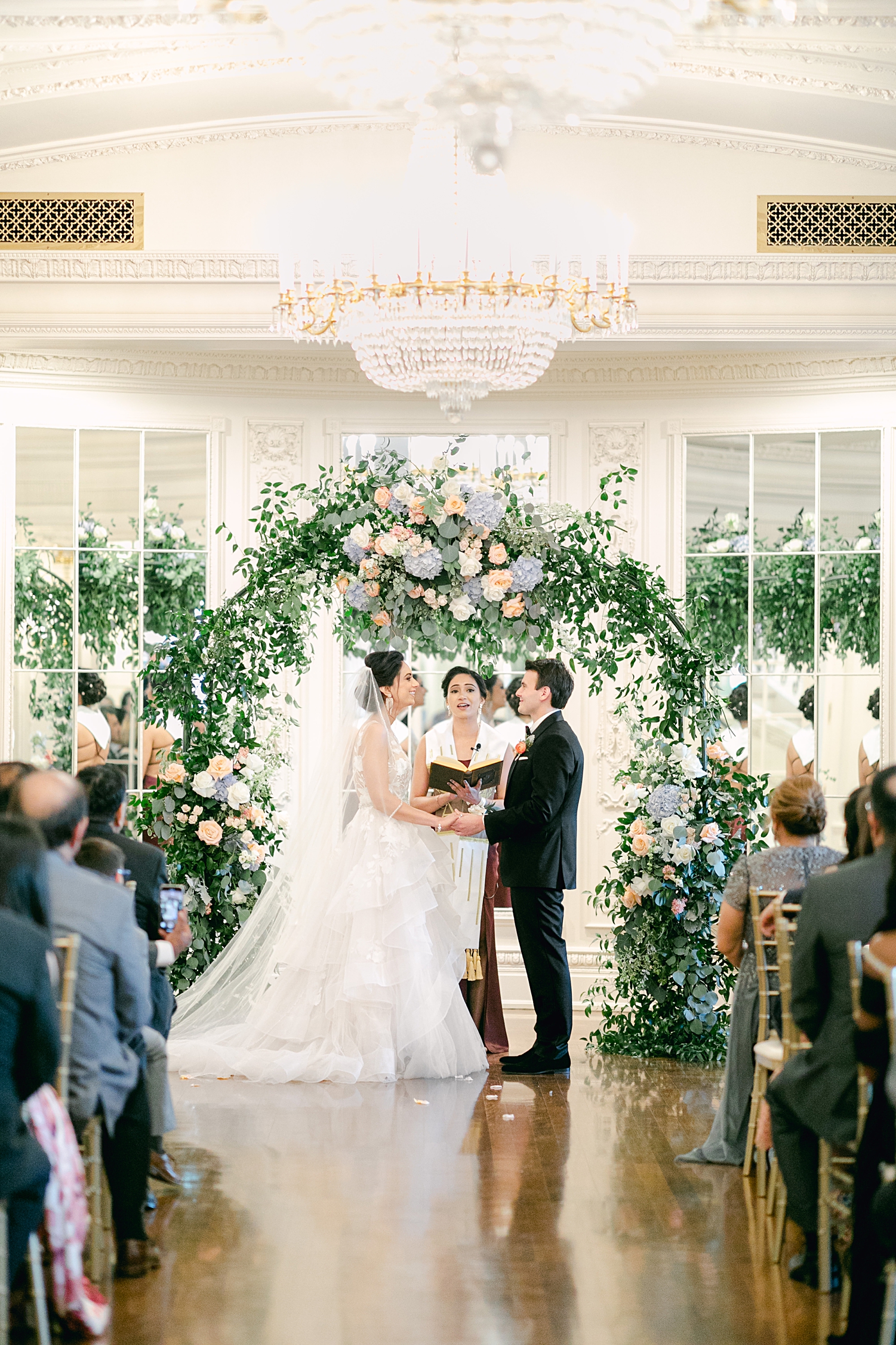Indoor french estate wedding ceremony bride and groom standing at altar under green flower arch