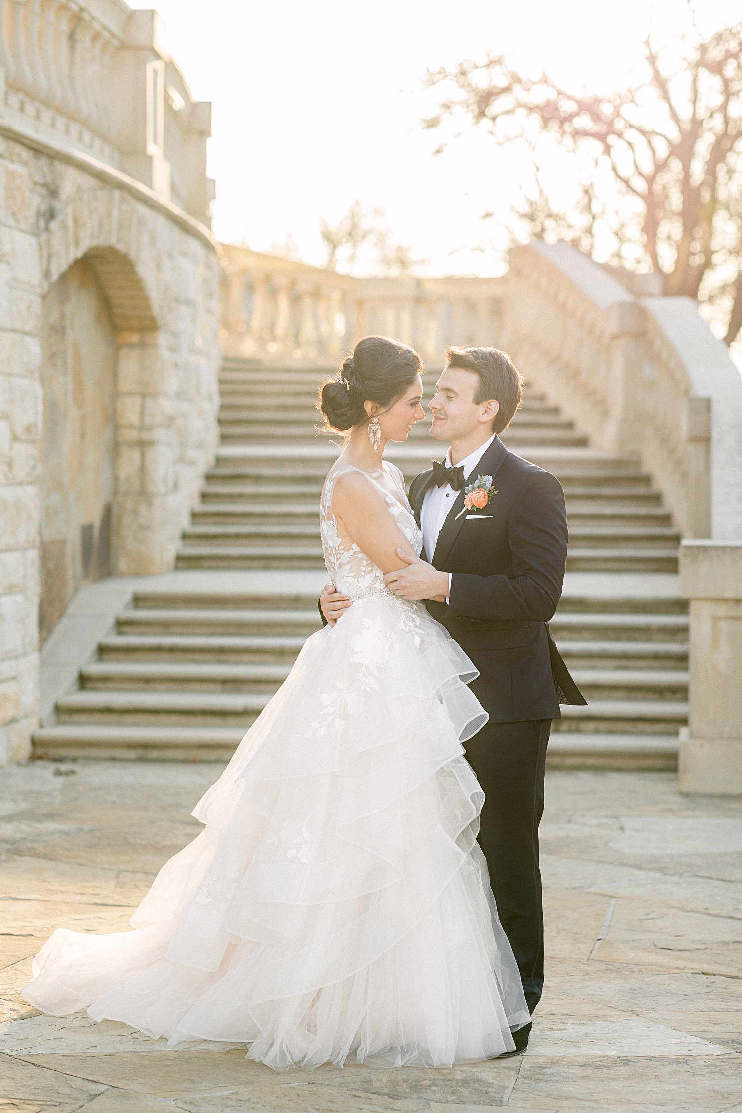 Bride and groom hugging in front of outdoor staircase at french estate wedding at sunset