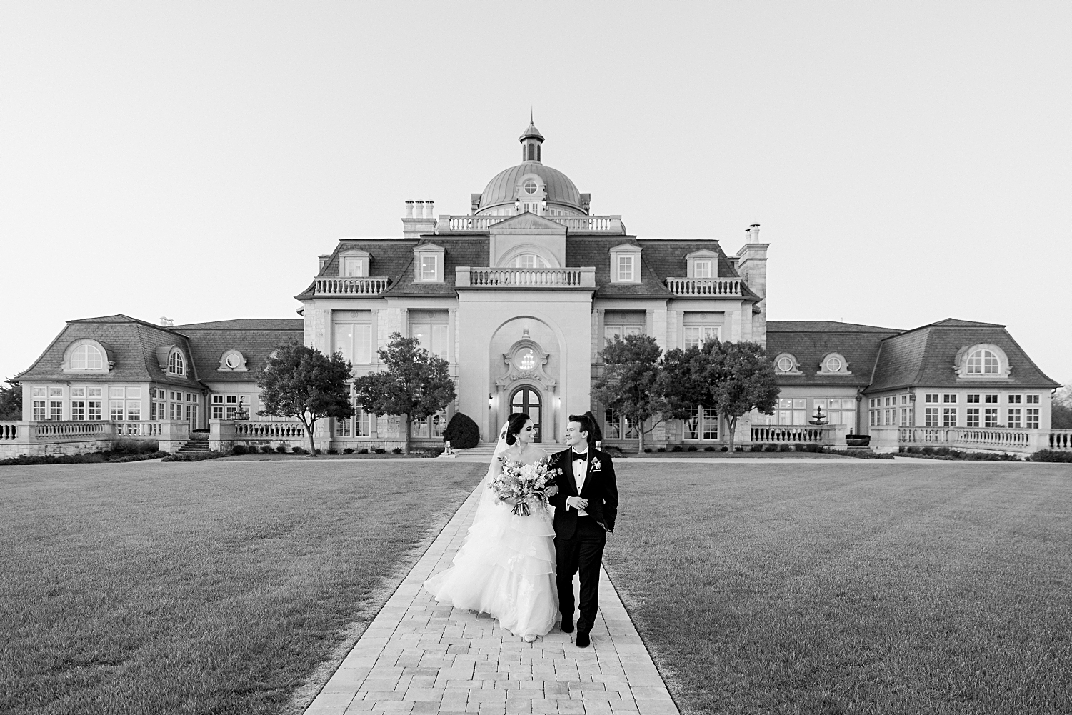 Bride and groom walking in front of mansion at french estate wedding at sunset black and white