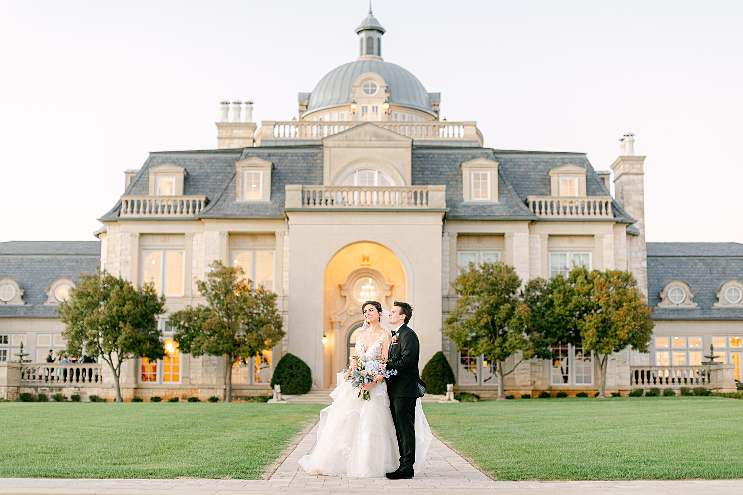 Bride and groom standing in front of mansion at french estate wedding at sunset