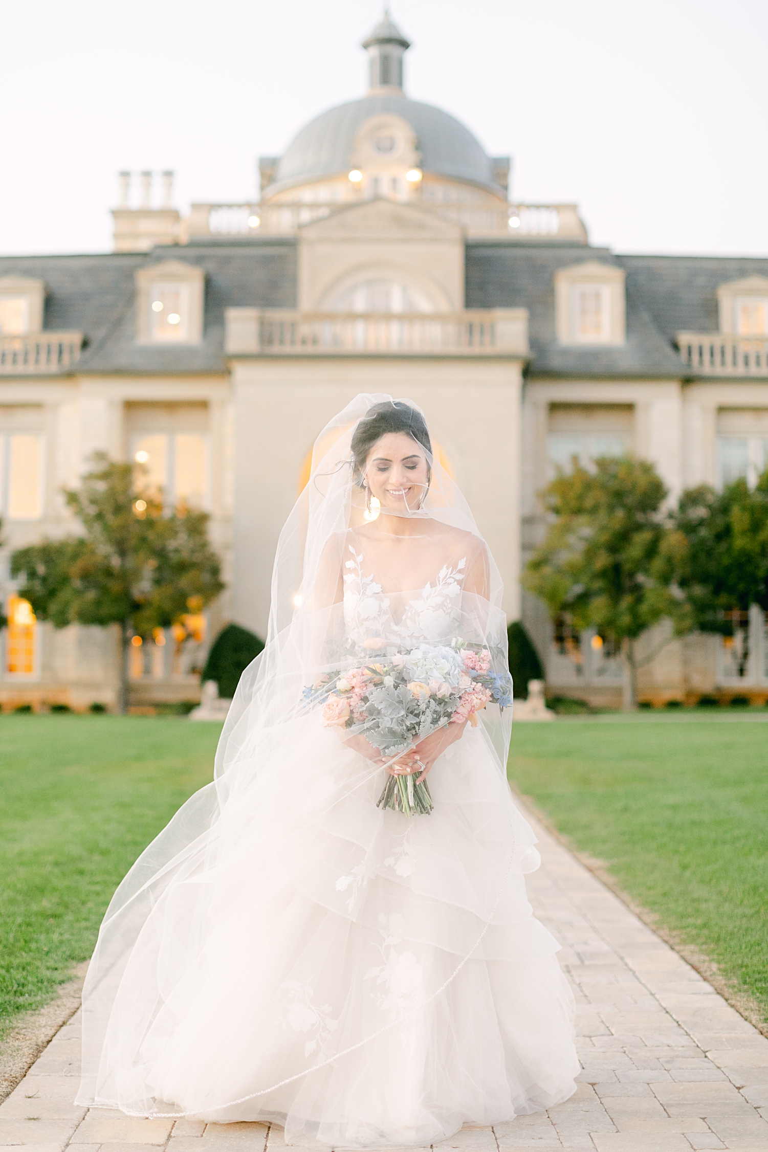 Bride holding bouquet in front of mansion at french estate wedding at sunset