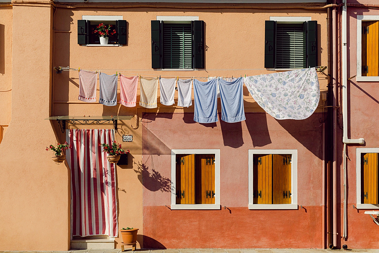 facade of orange two story home in Burano Italy with line of laundry hanging