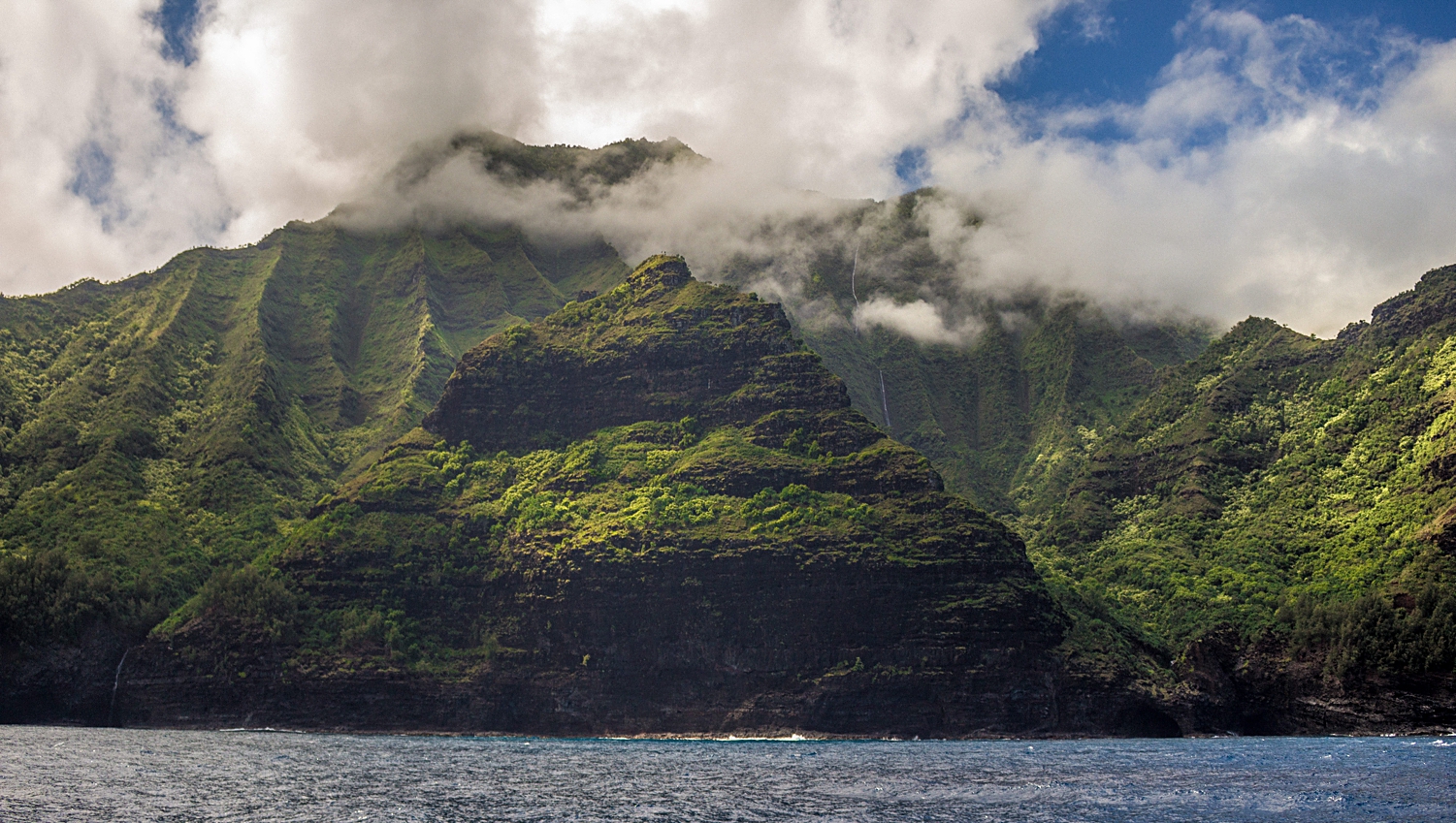 Green sea cliffs rising from ocean into clouds in hawaii