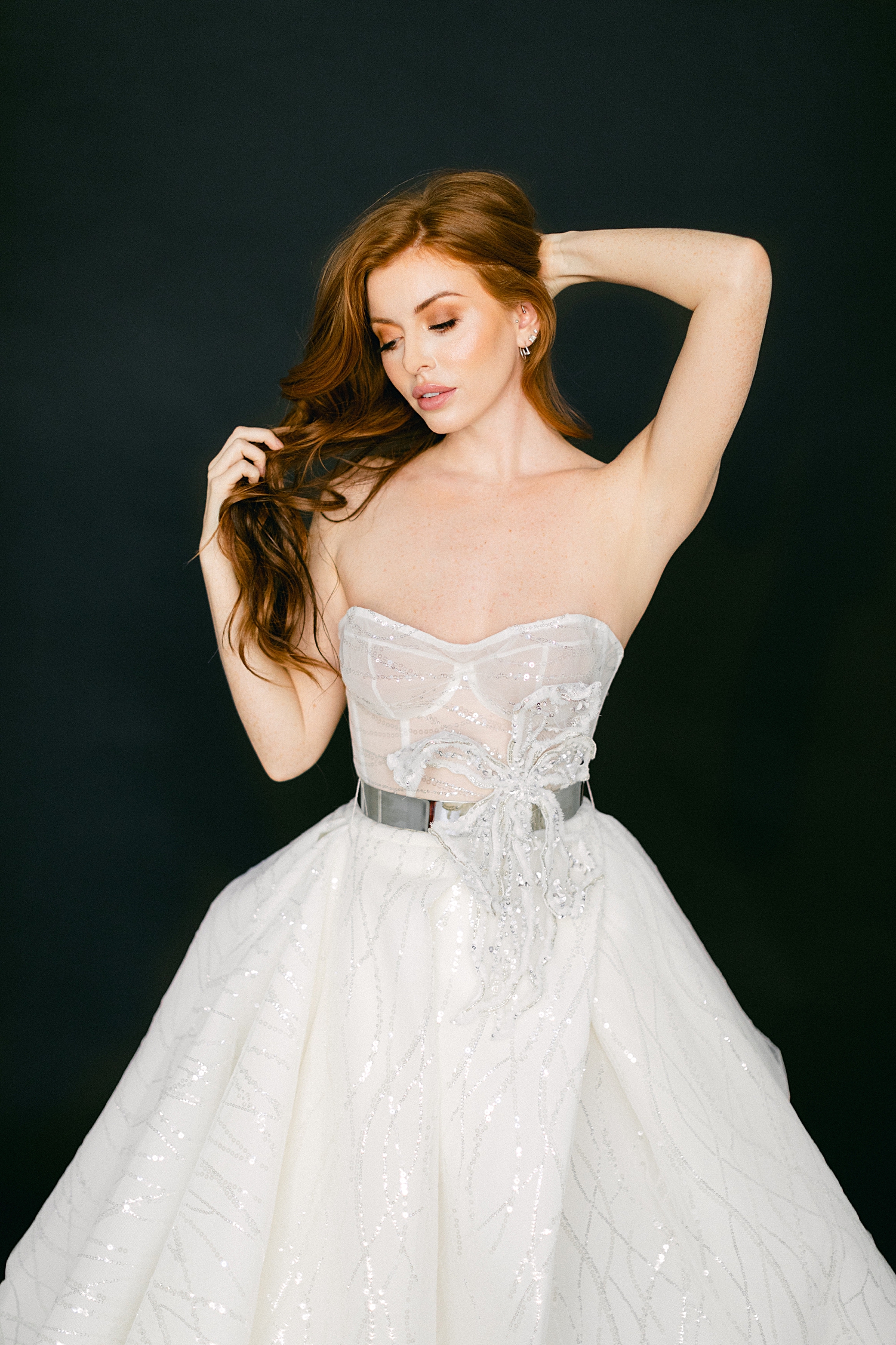 red headed girl with hands in hair wearing sparkling white wedding gown