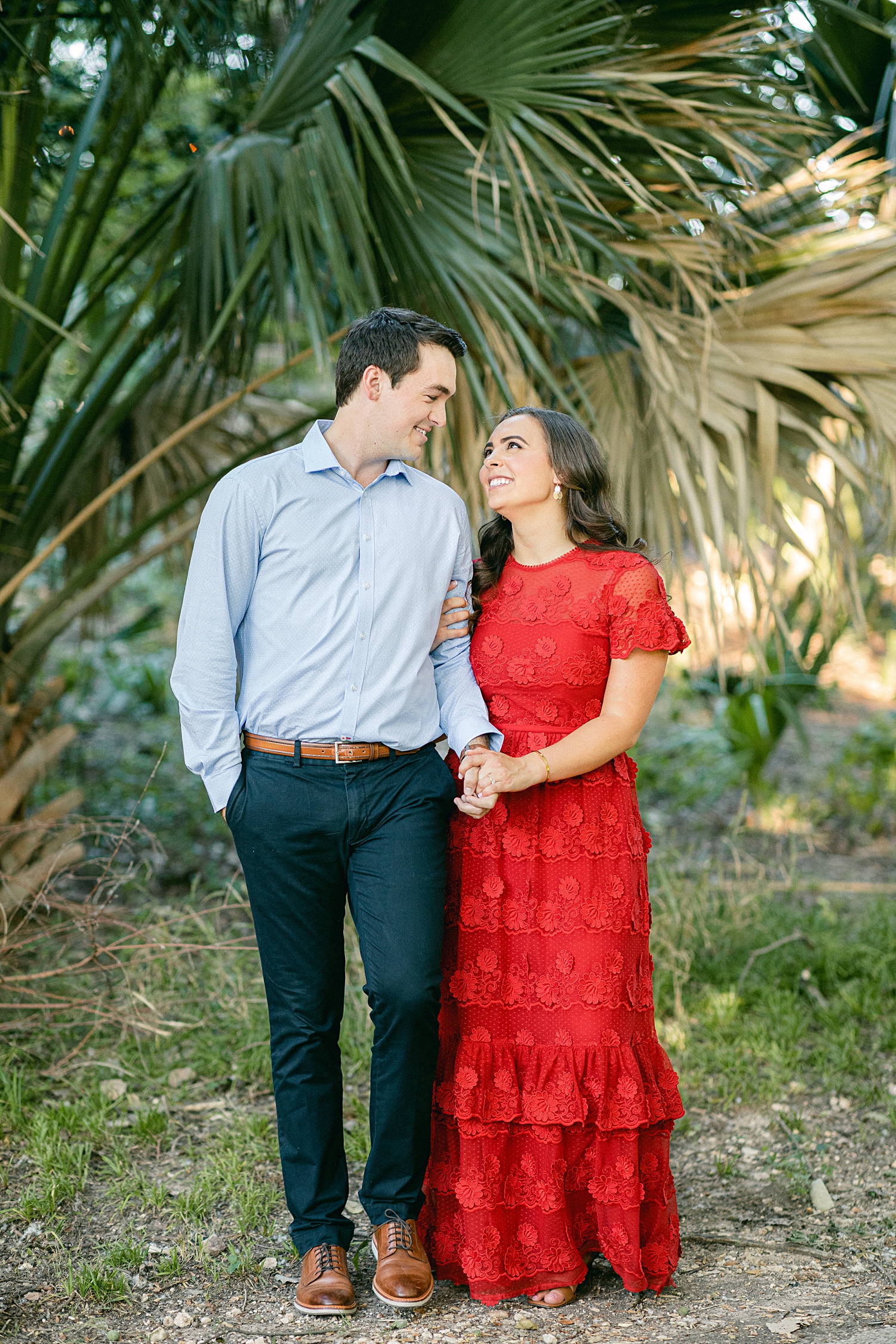 Man and woman in red dress walking in green garden Austin engagement at Laguna Gloria