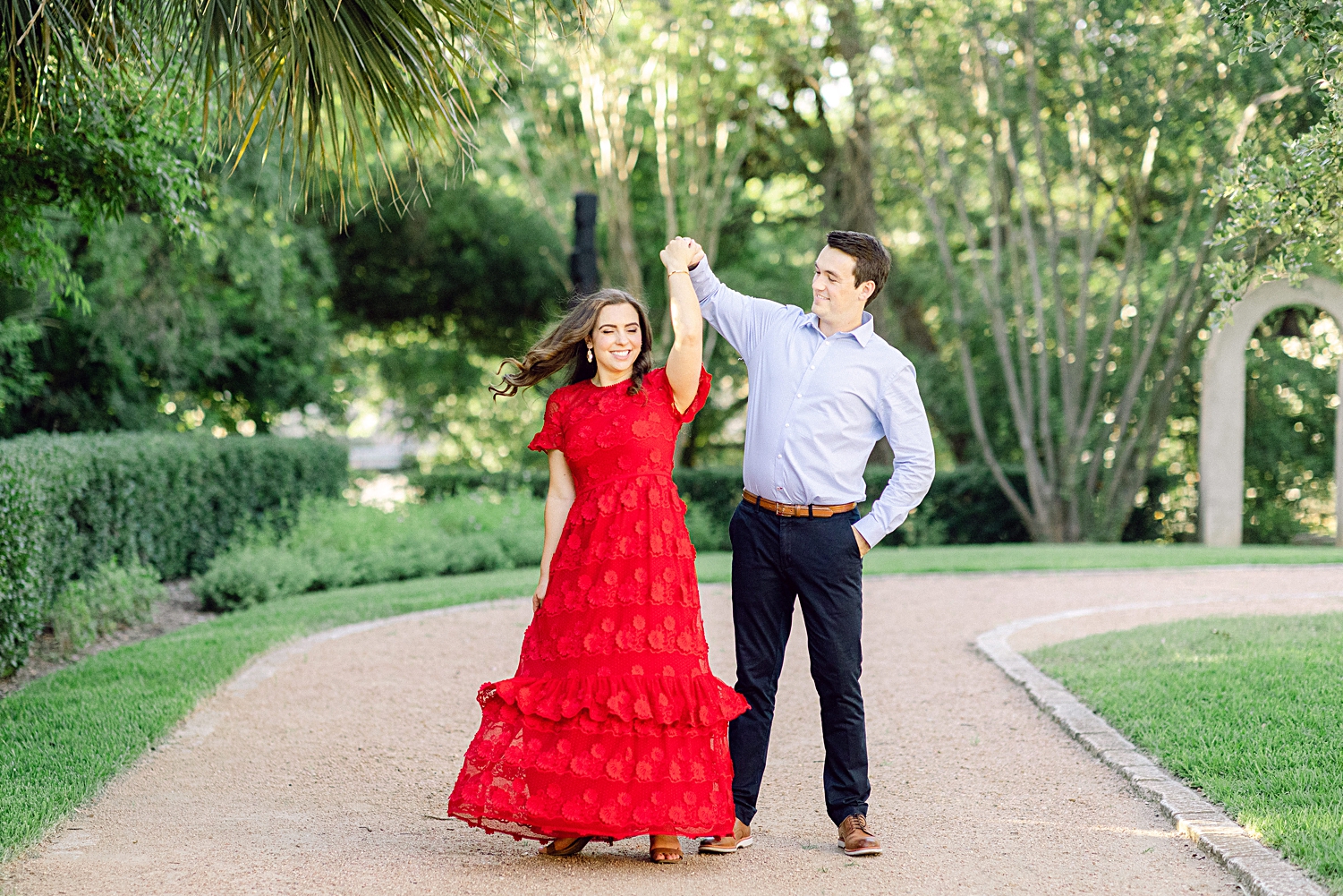 Man and woman in red dress dancing in green garden Austin engagement at Laguna Gloria