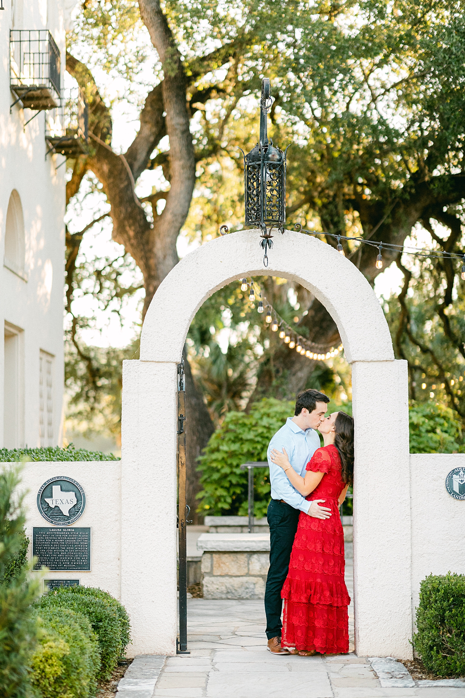 Man and woman in red dress kissing under archway Austin engagement at Laguna Gloria