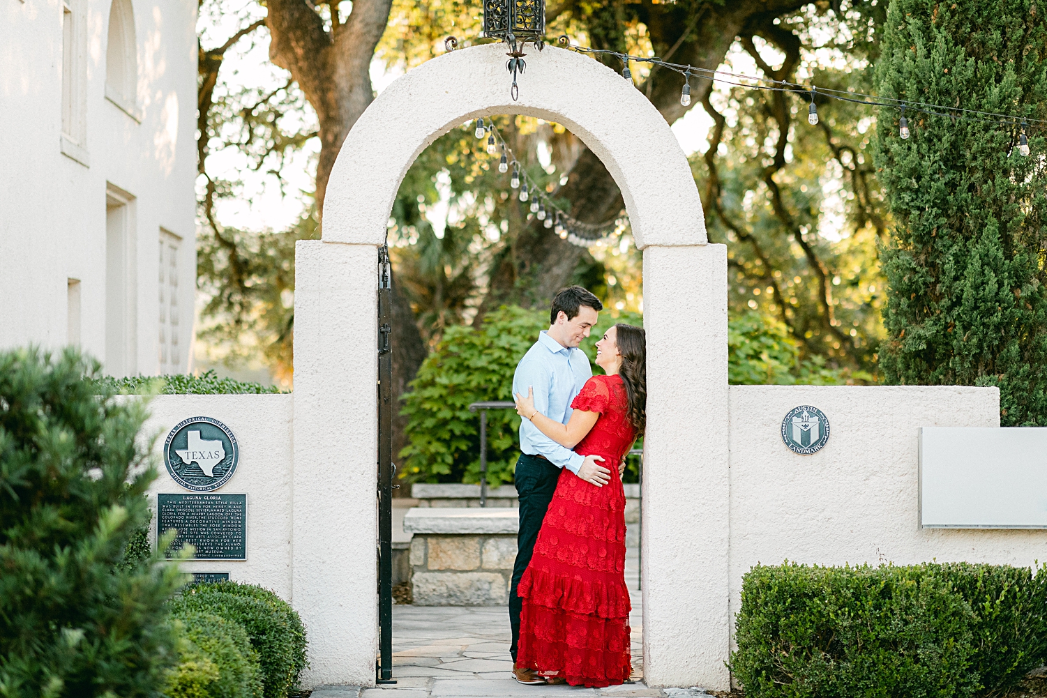 Man and woman in red dress embracing under archway Austin Laguna Gloria