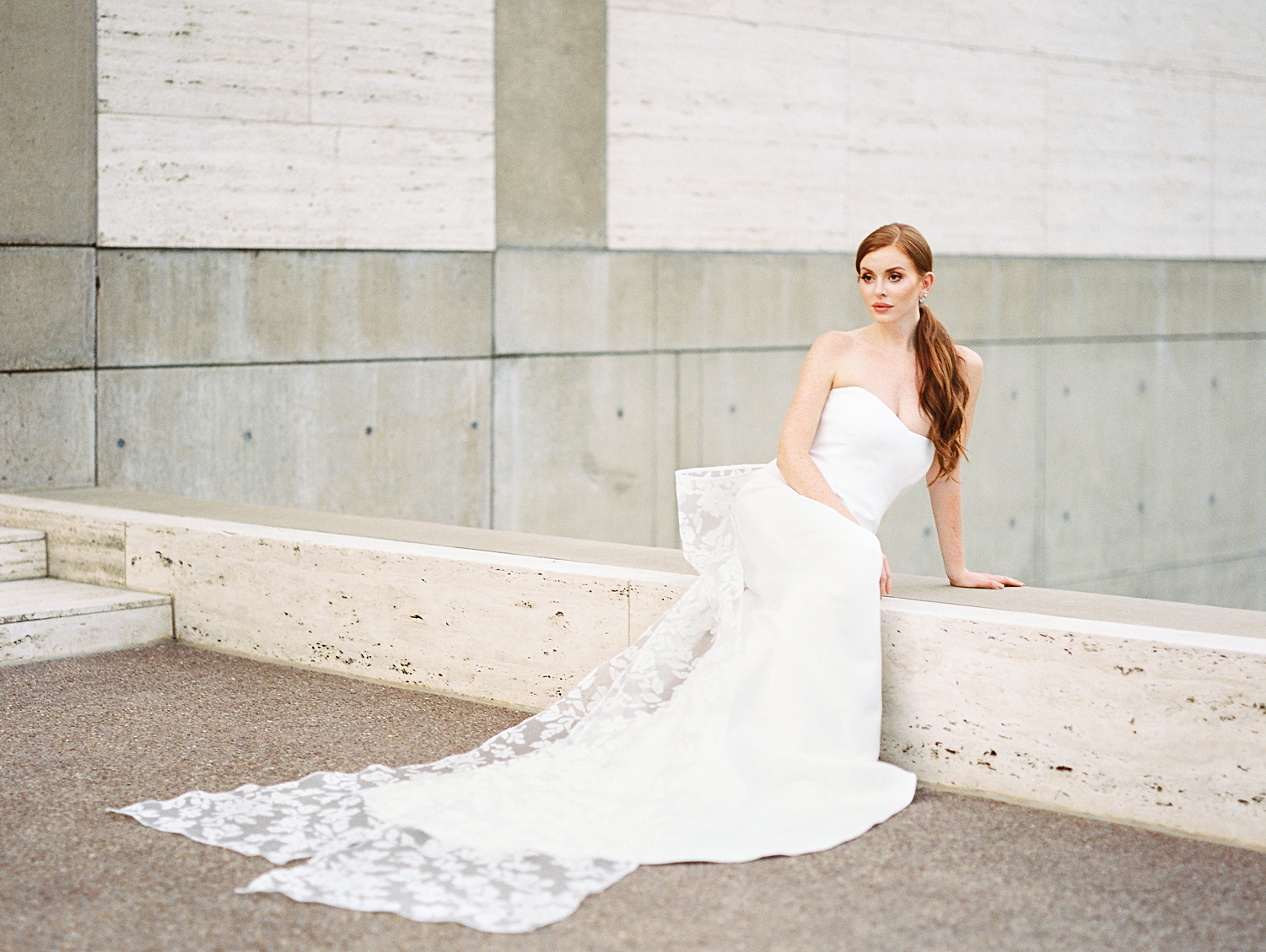 red headed bride in white wedding gown with lace bow on back sitting on ledge
