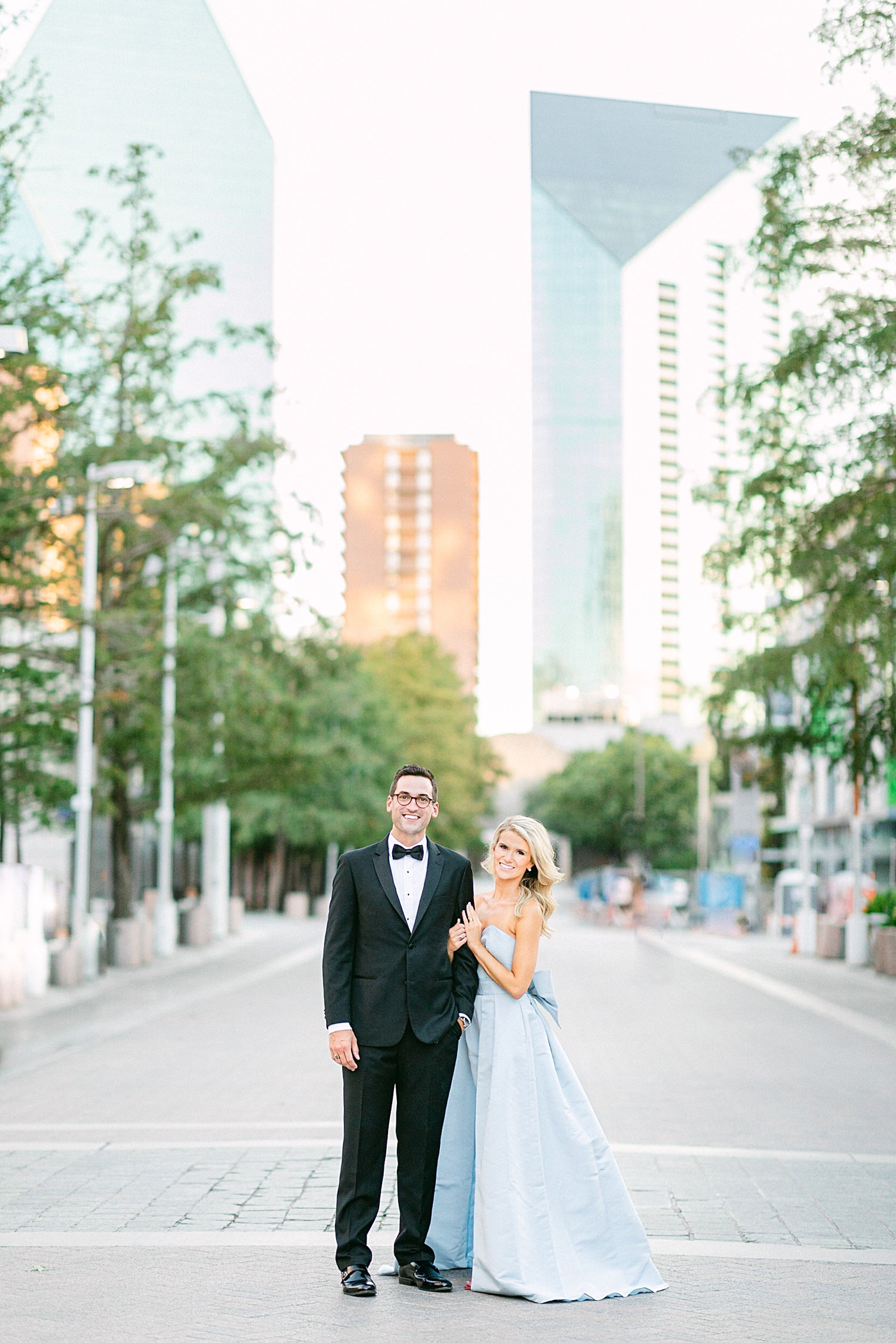 Man in black tuxedo and woman in light blue jumpsuit standing together in Dallas street