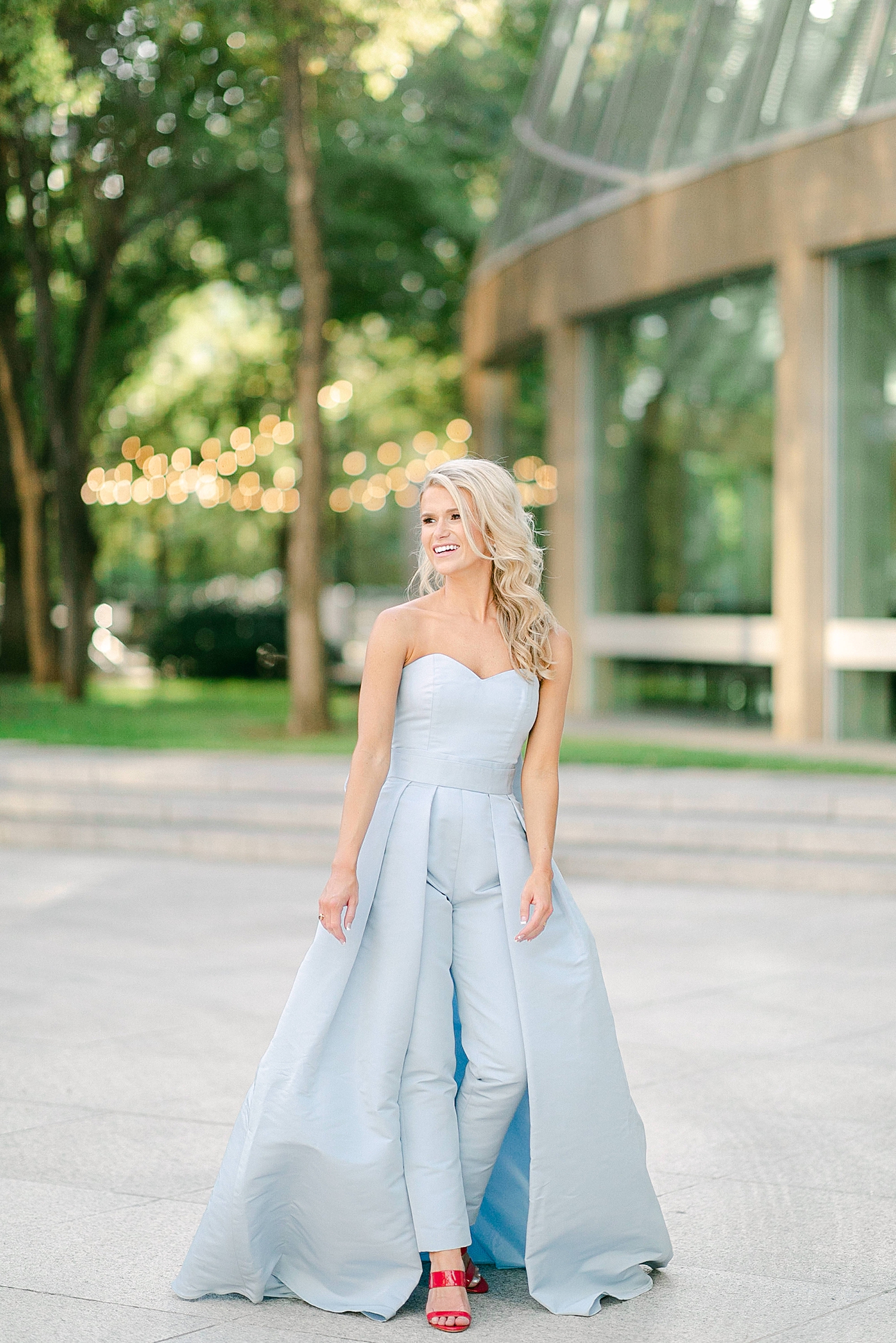 woman in light blue jumpsuit with skirt standing by green garden in downtown Dallas