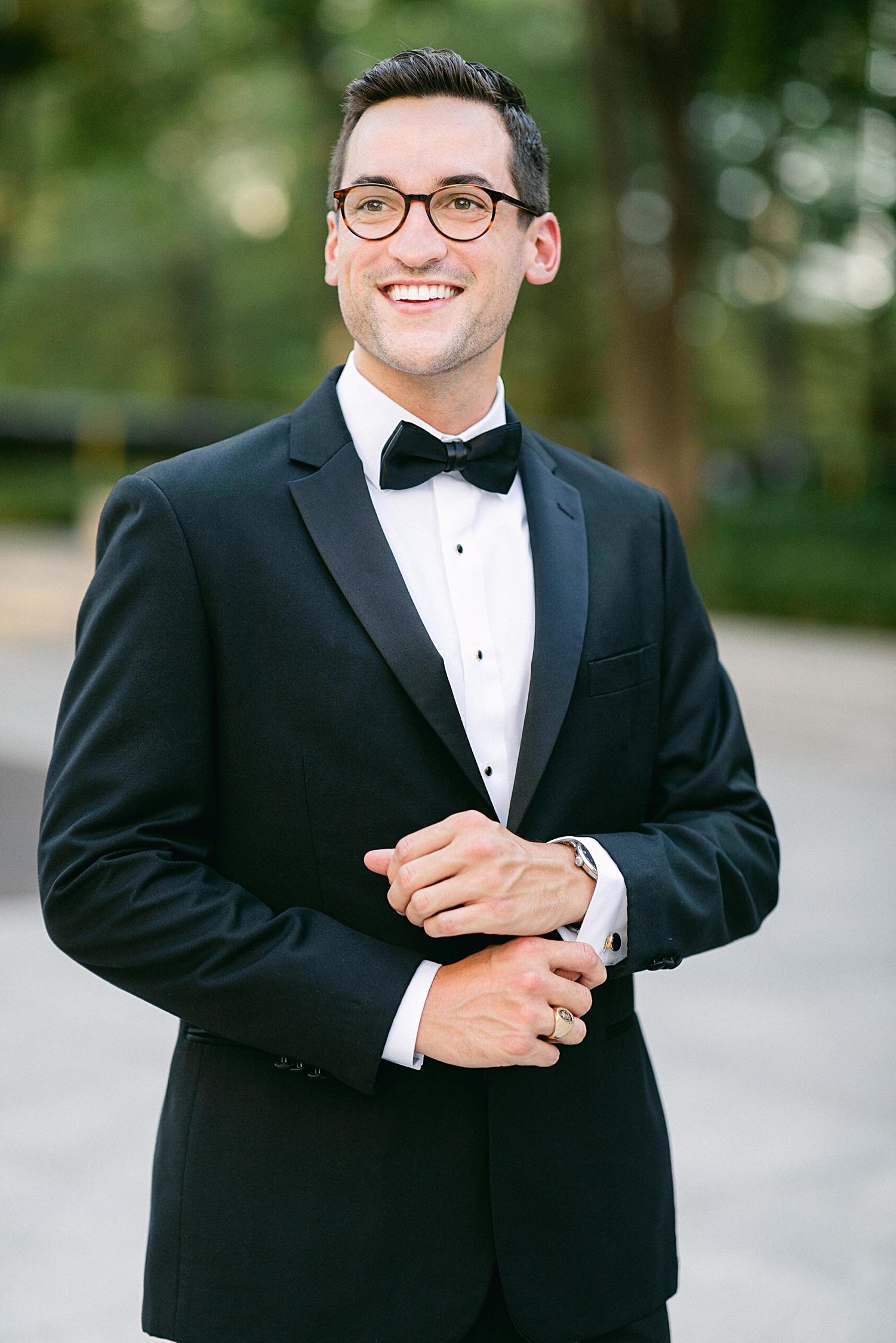 Man in black tuxedo smiling and adjusting cuffs