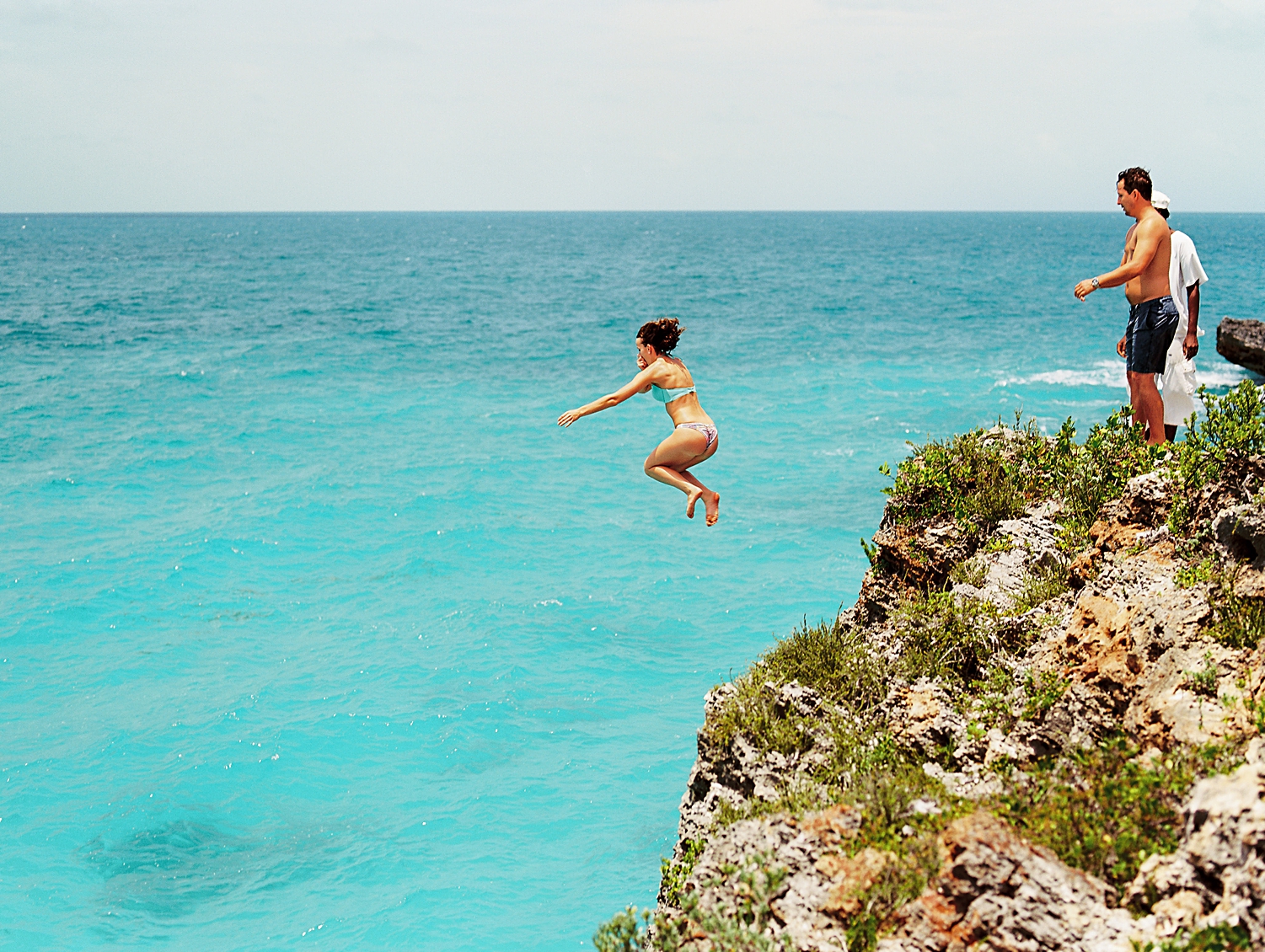 woman cliff jumping into turquoise ocean Bahamas 