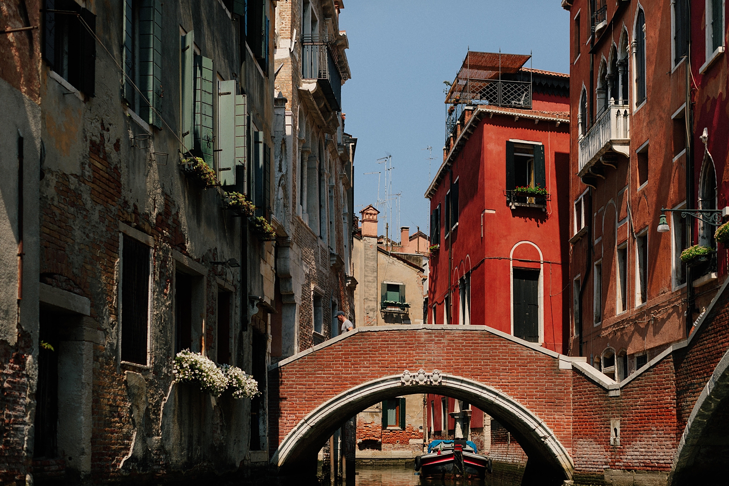 Venice Canal scene with red building and brick bridge under a blue sky