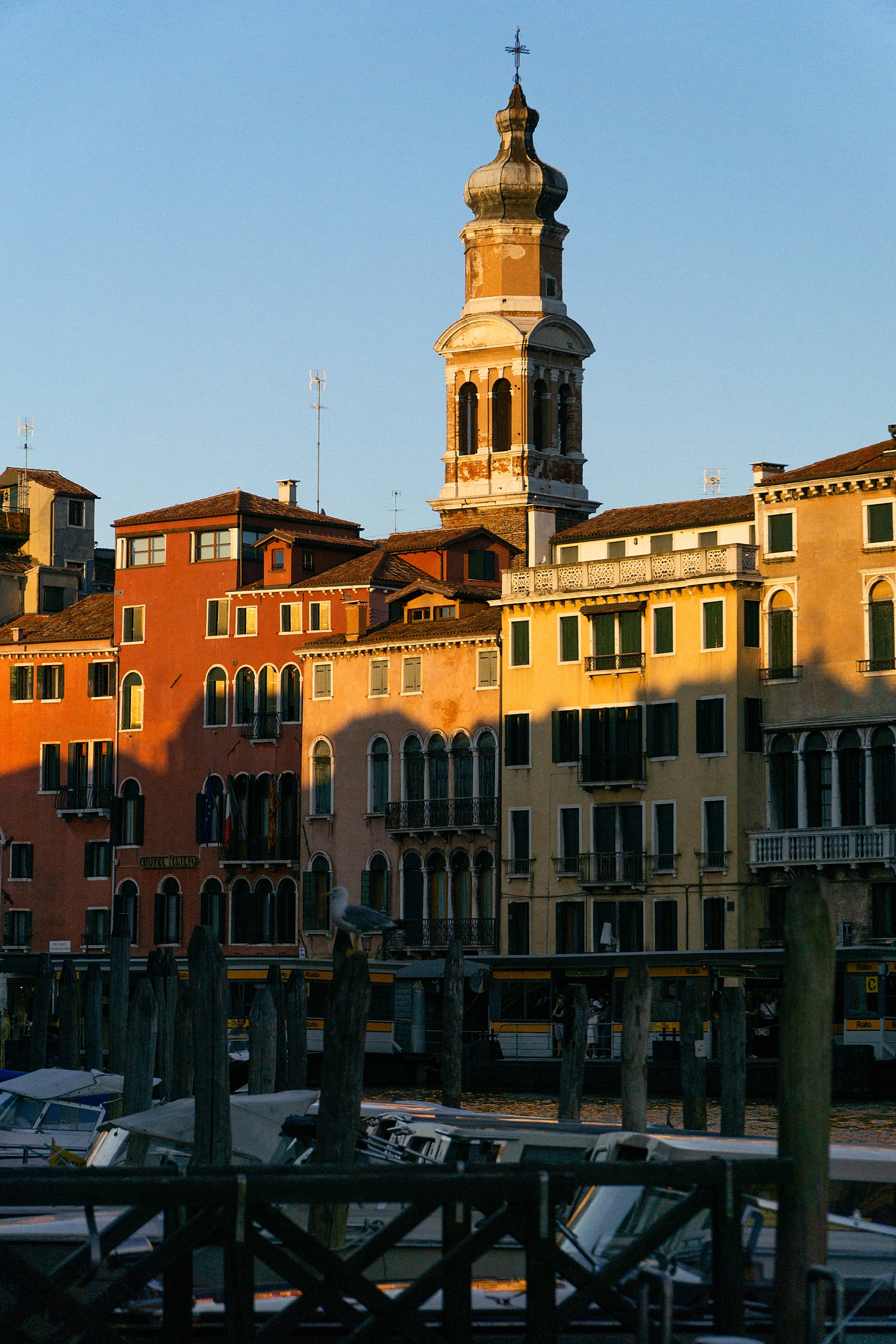Grand Canal orange and yellow buildings with Chiesa Cattolica Parrocchiale dei Santi Apostoli Tower at sunset in Venice, Italy 