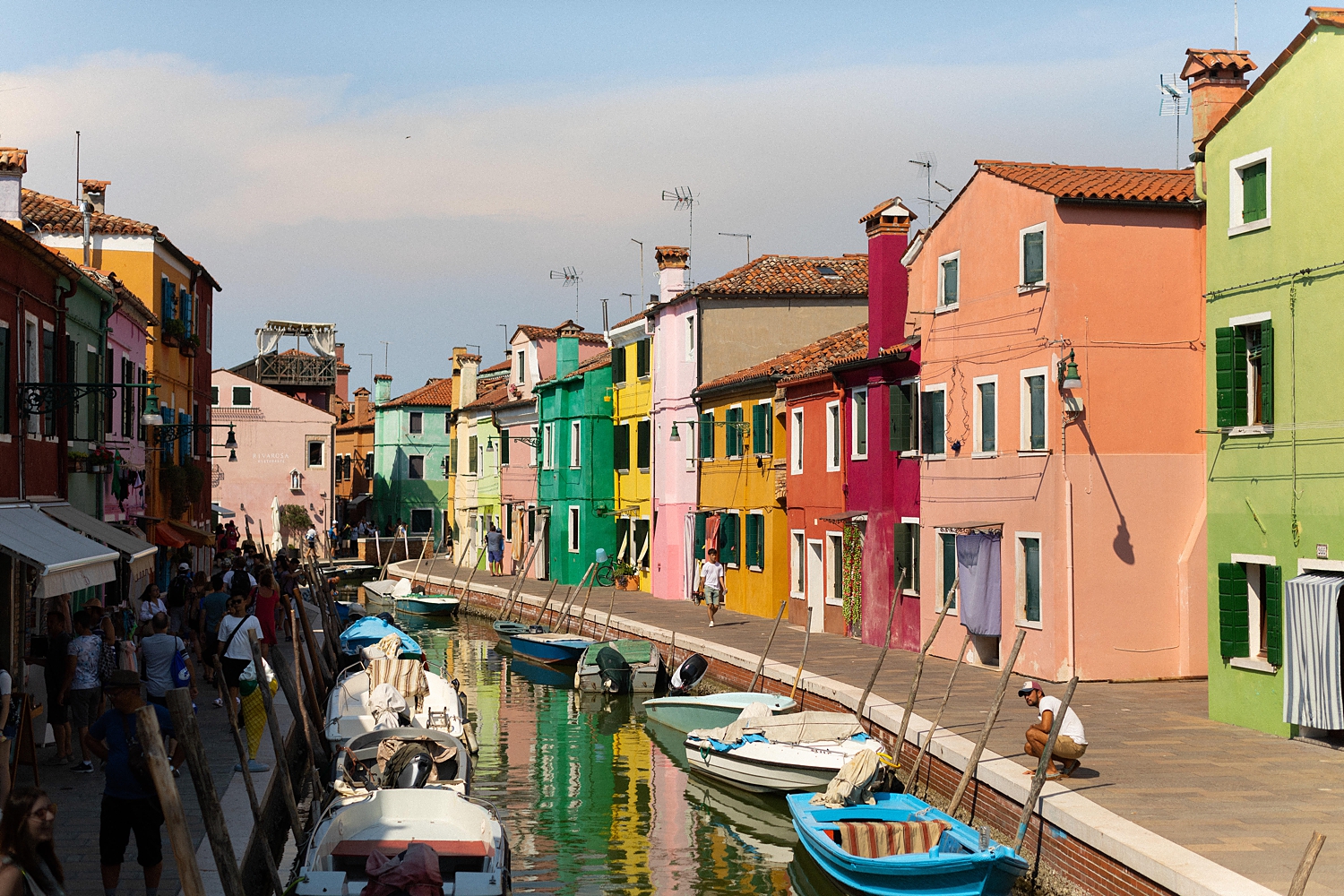 Canal and colorful street scene in Burano, Italy against blue sky
