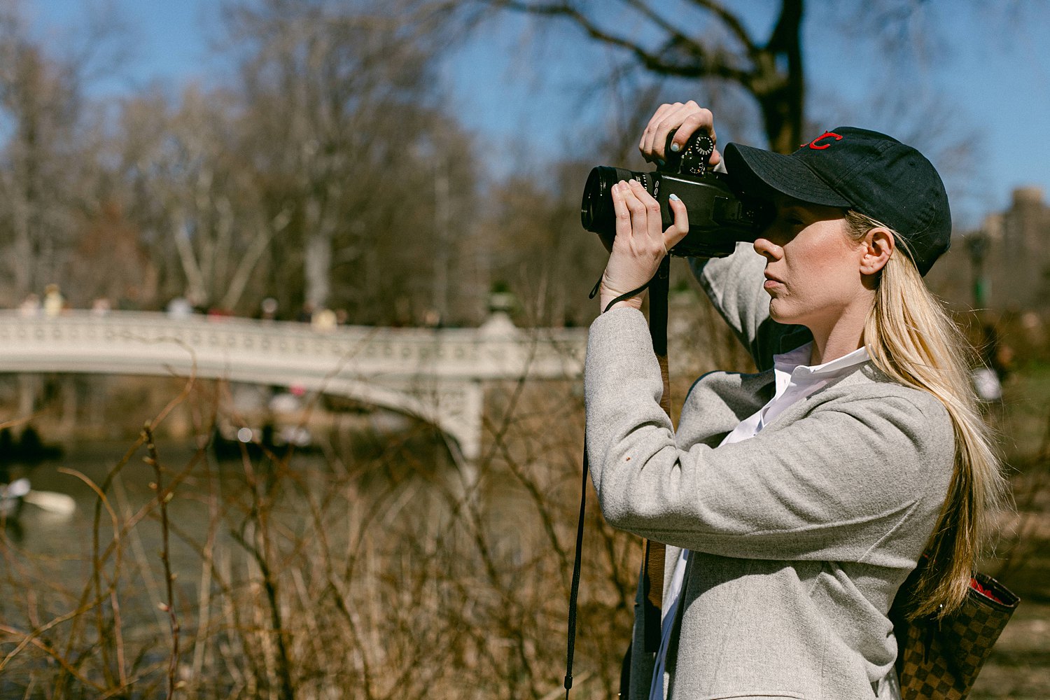 Woman in baseball cap holding camera up to eye in Central Park NYC