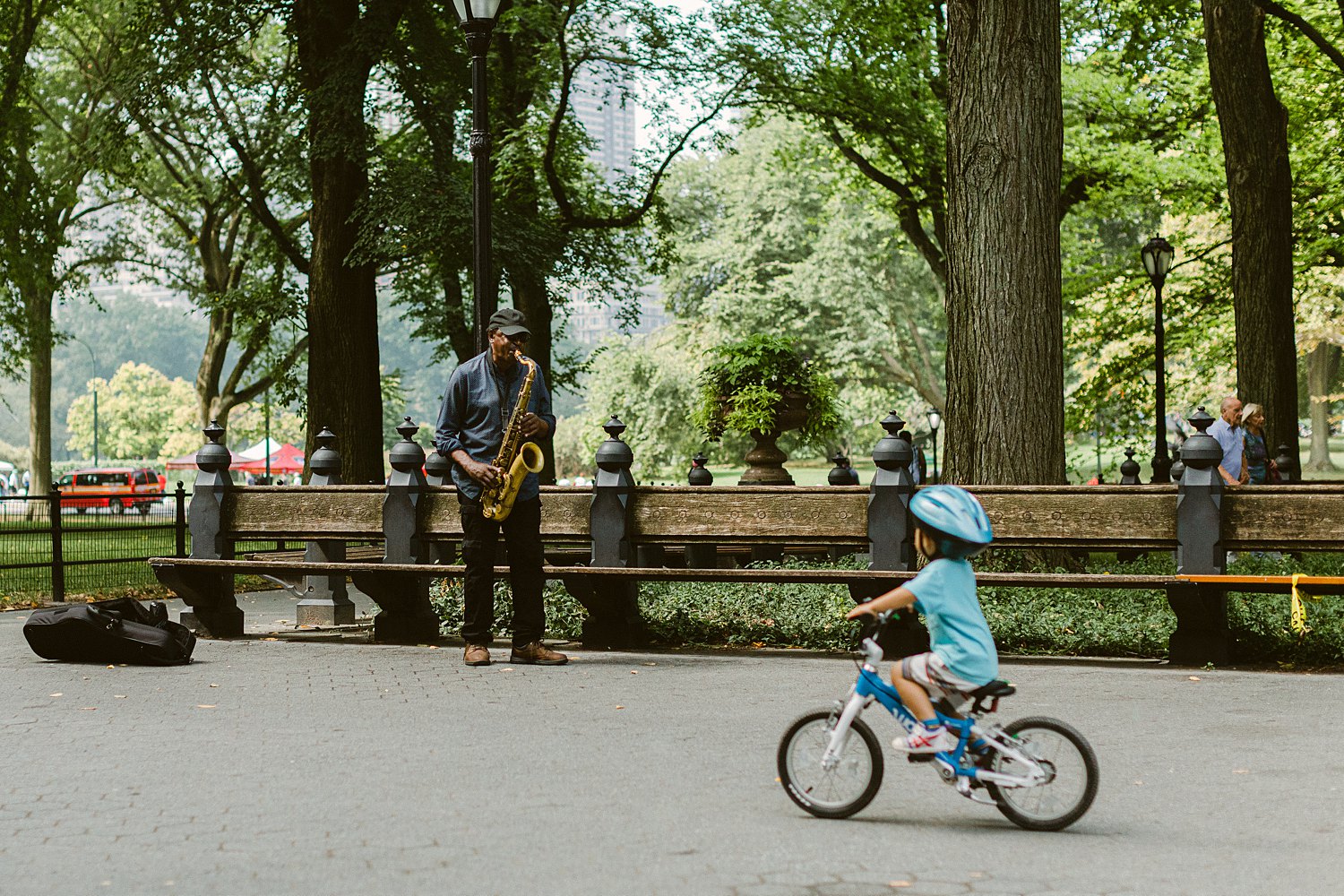 small child on bike passing man playing saxophone in central park nyc