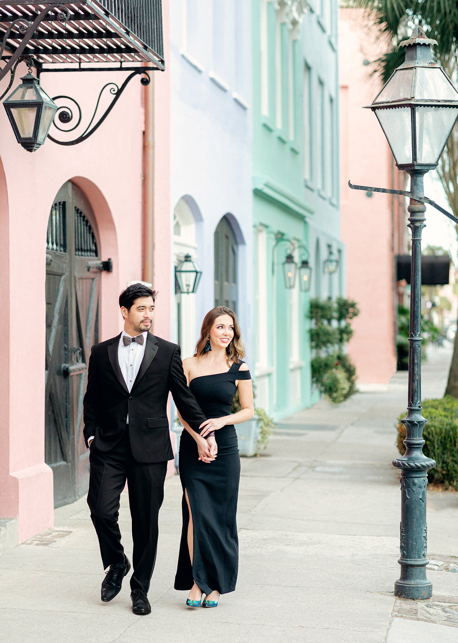 Man in tuxedo and girl in black dress walking by rainbow row homes