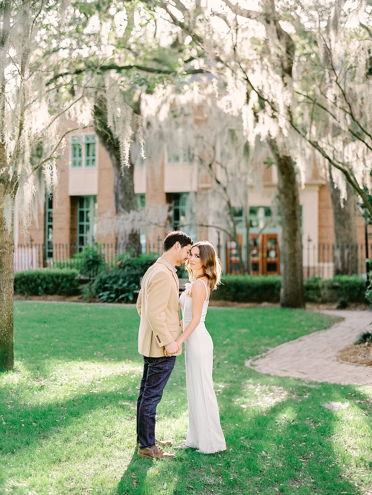 Couple holding hands together on green lawn under mossy trees at the College of Charleston