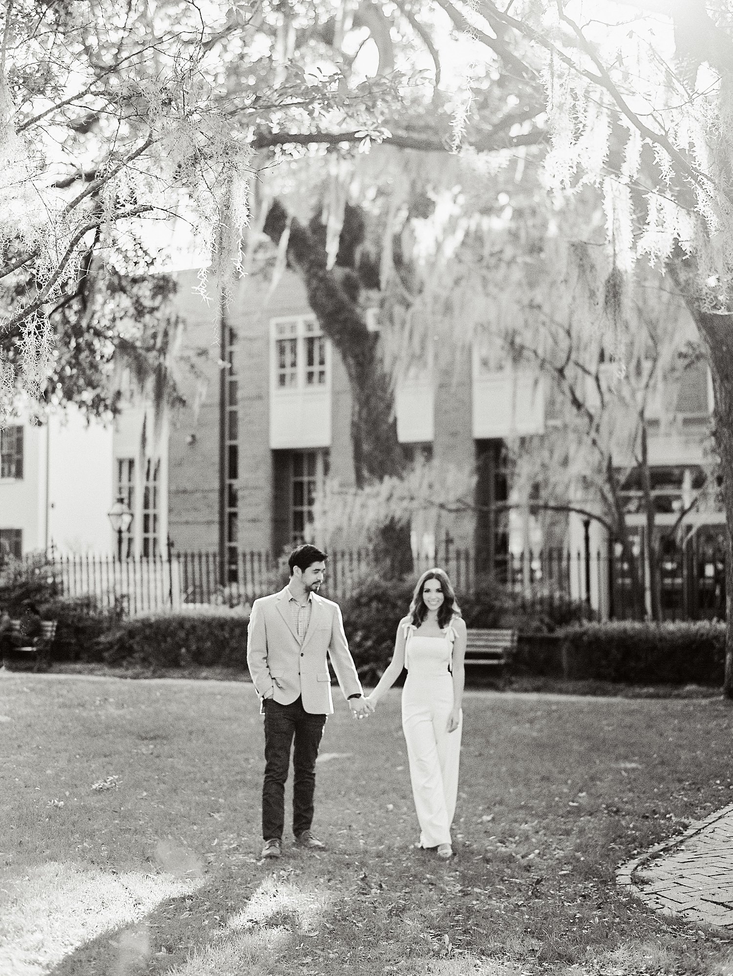 Couple holding hands lawn under mossy trees at the College of Charleston