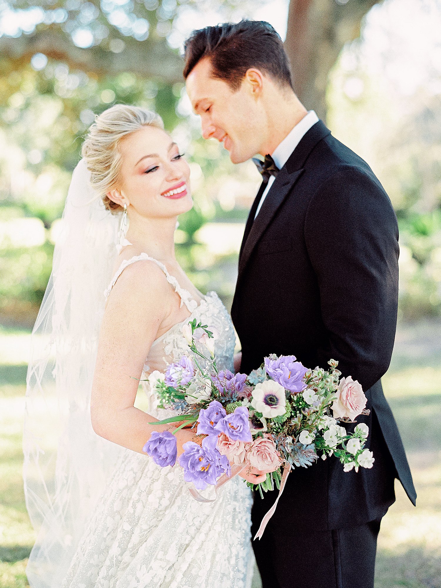 Bride and groom embracing with purple floral bouquet laughing outside wedding Charleston