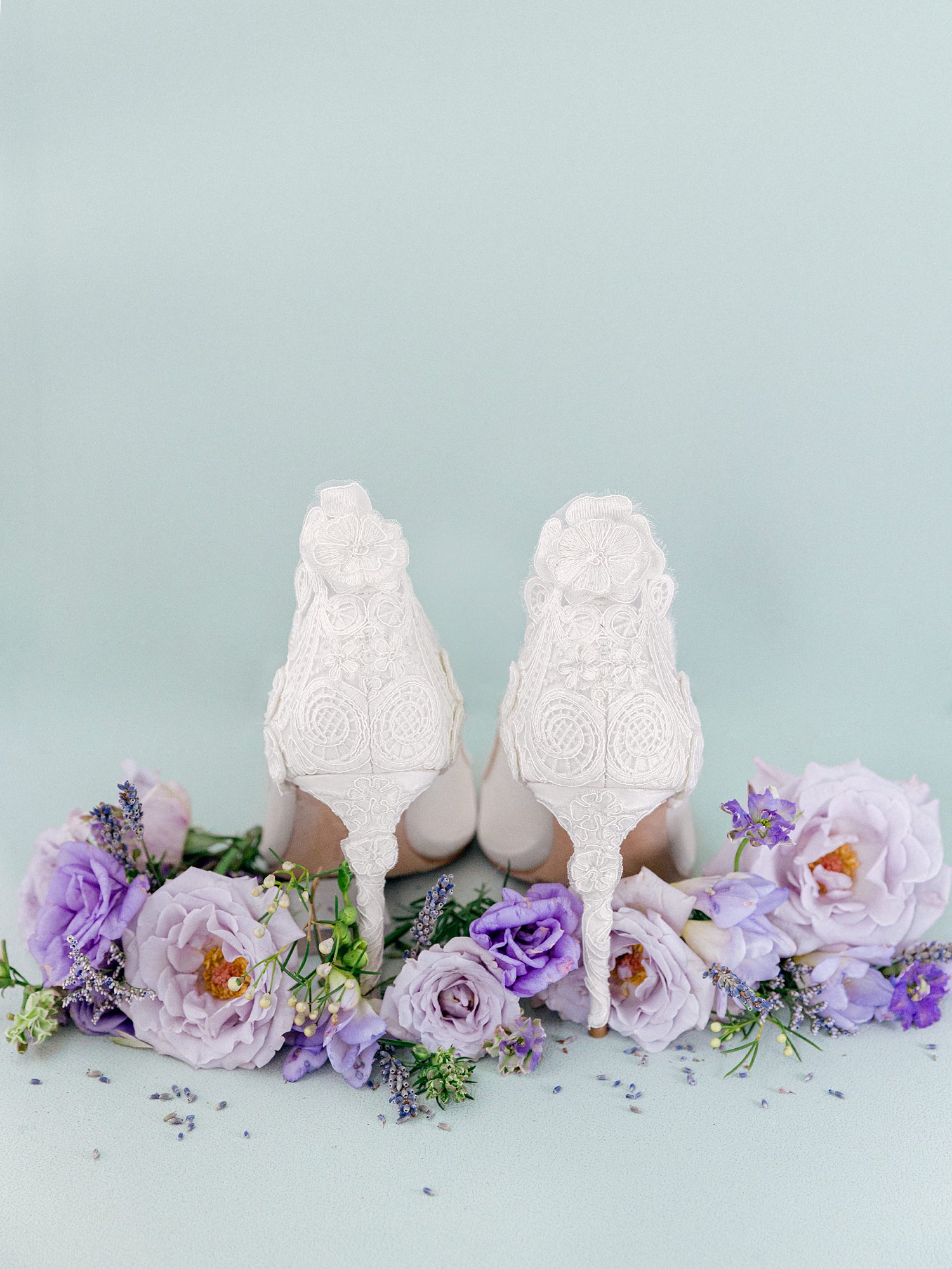 white high heel bridal shoes among purple flowers against green backdrop