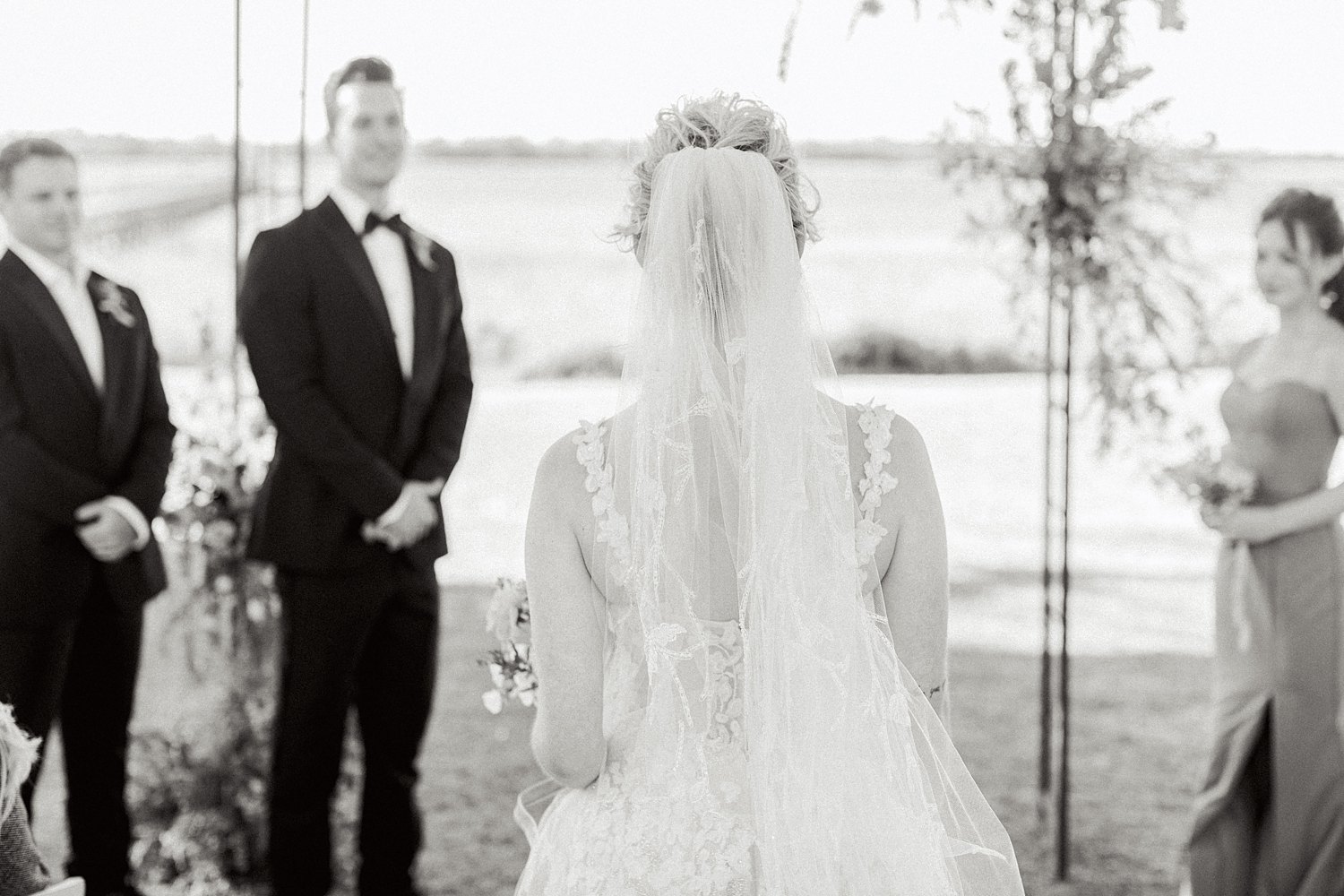 bride walking down aisle to groom in tuxedo at outdoor ceremony at Lowndes Grove Charleston wedding black and white