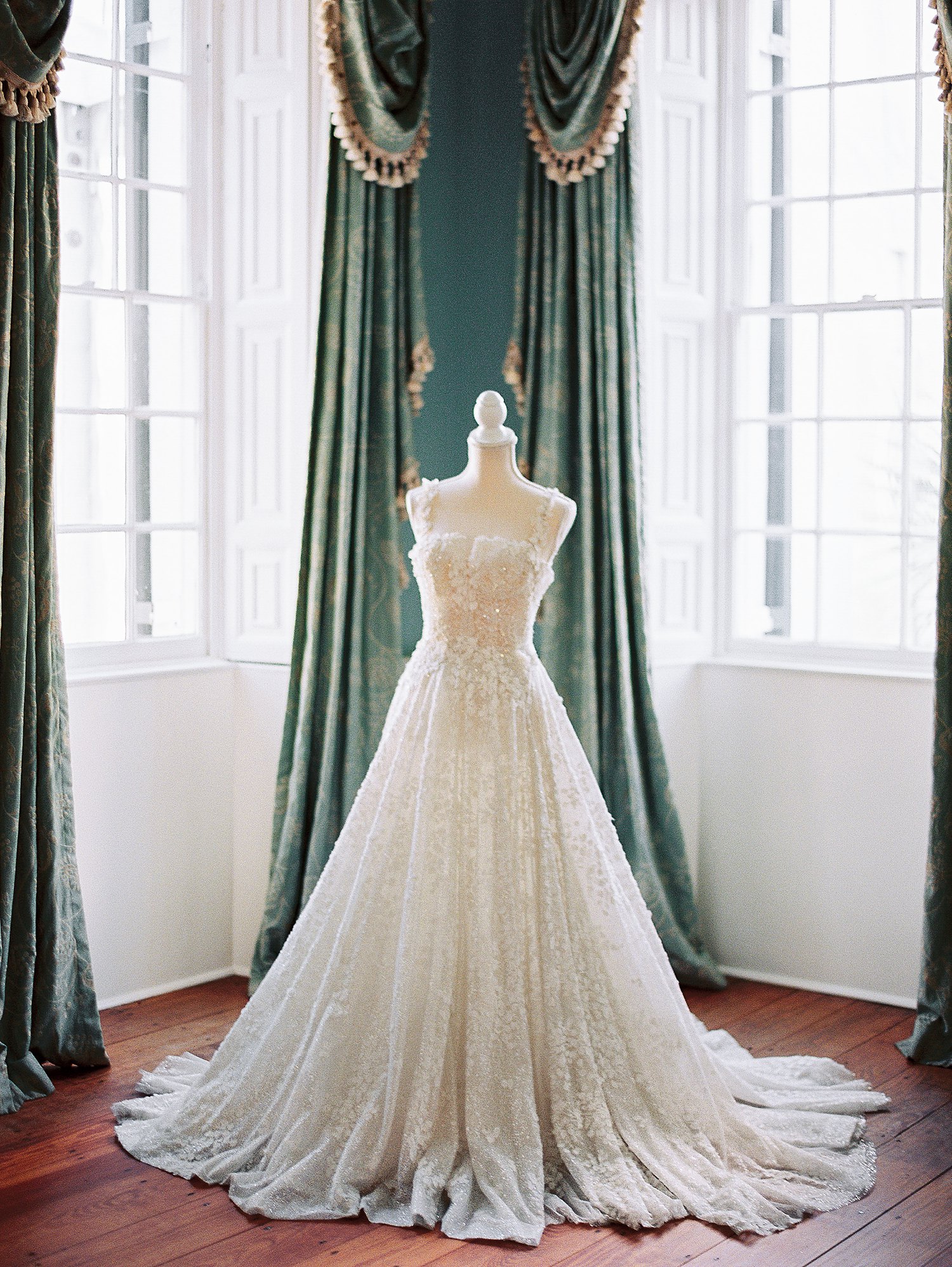 white wedding dress on bust in front of green curtains and windows