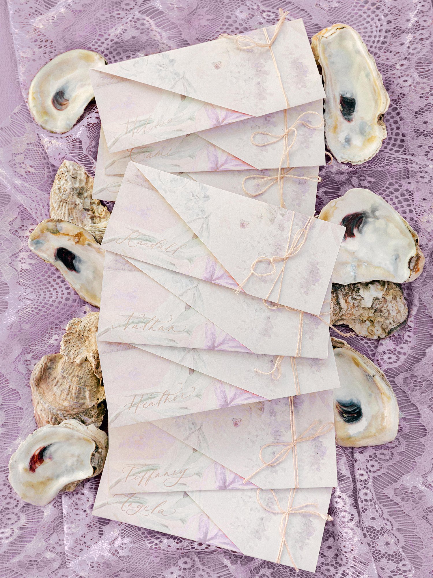 Oyster shells surrounding folded menus against purple lace backdrop wedding flat lay