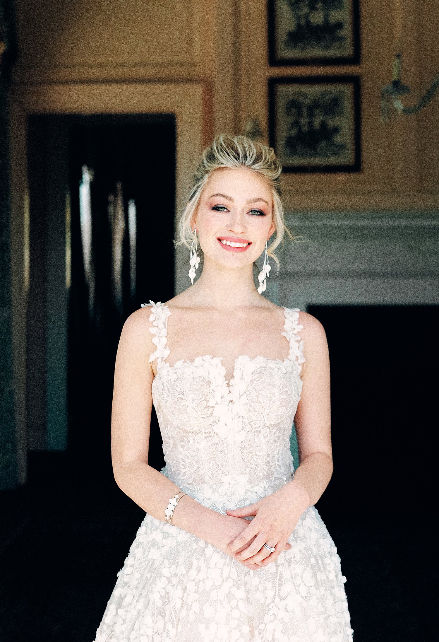 portrait of bride in white wedding dress smiling with hands clasped