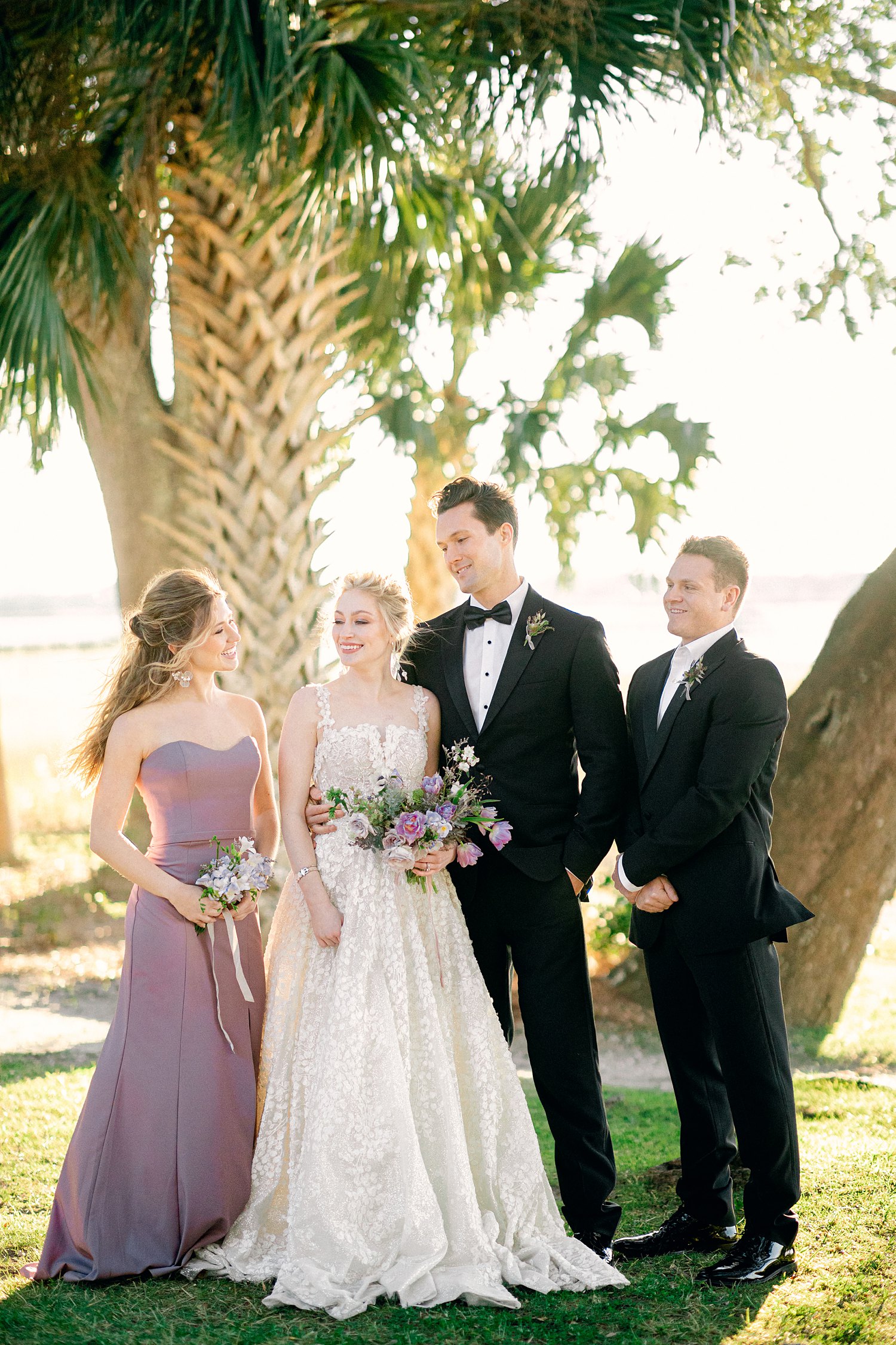 Bride and groom with maid of honor and best man by trees outside wedding