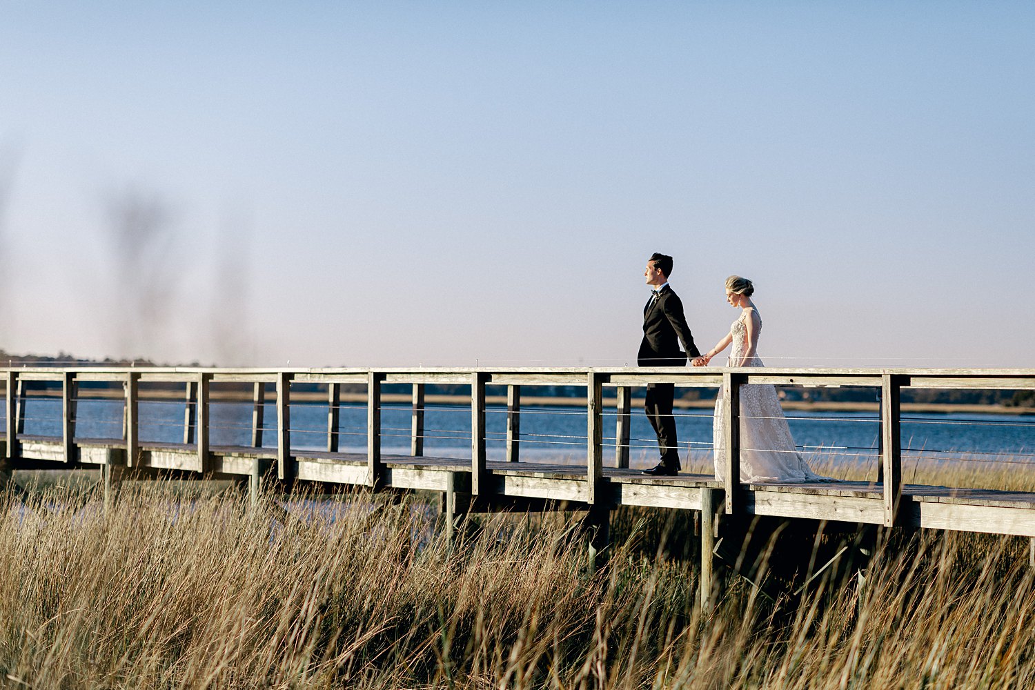 Bride and groom walking down wooden dock on river at Charleston Wedding