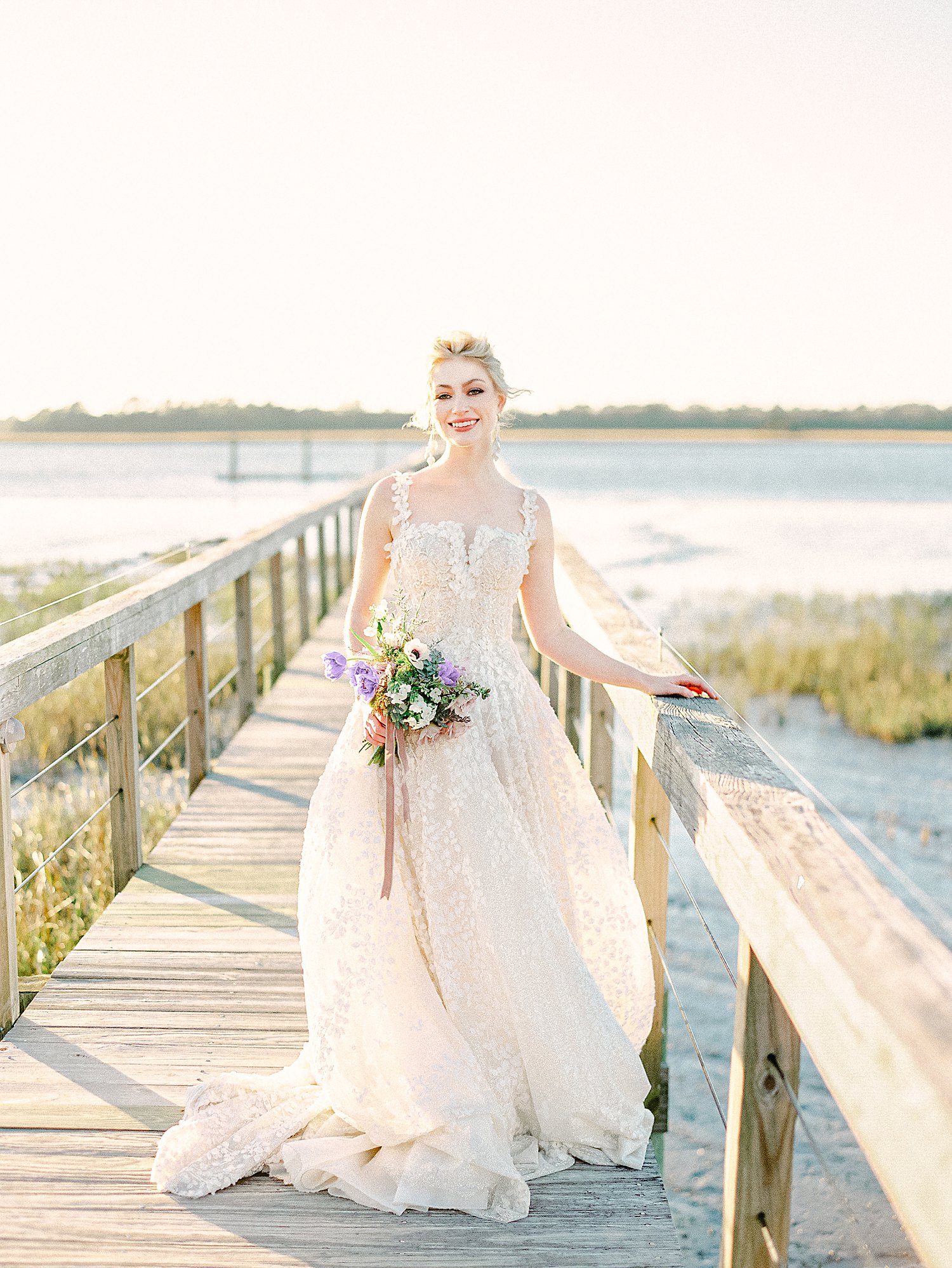 Bride with purple floral bouquet smiling on wooden dock on river at Charleston Wedding